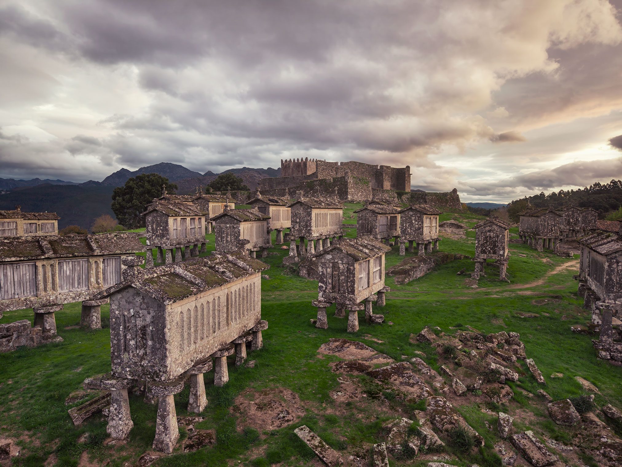 Rows of old stone granaries on stone stilts before a castle wall in Portugal