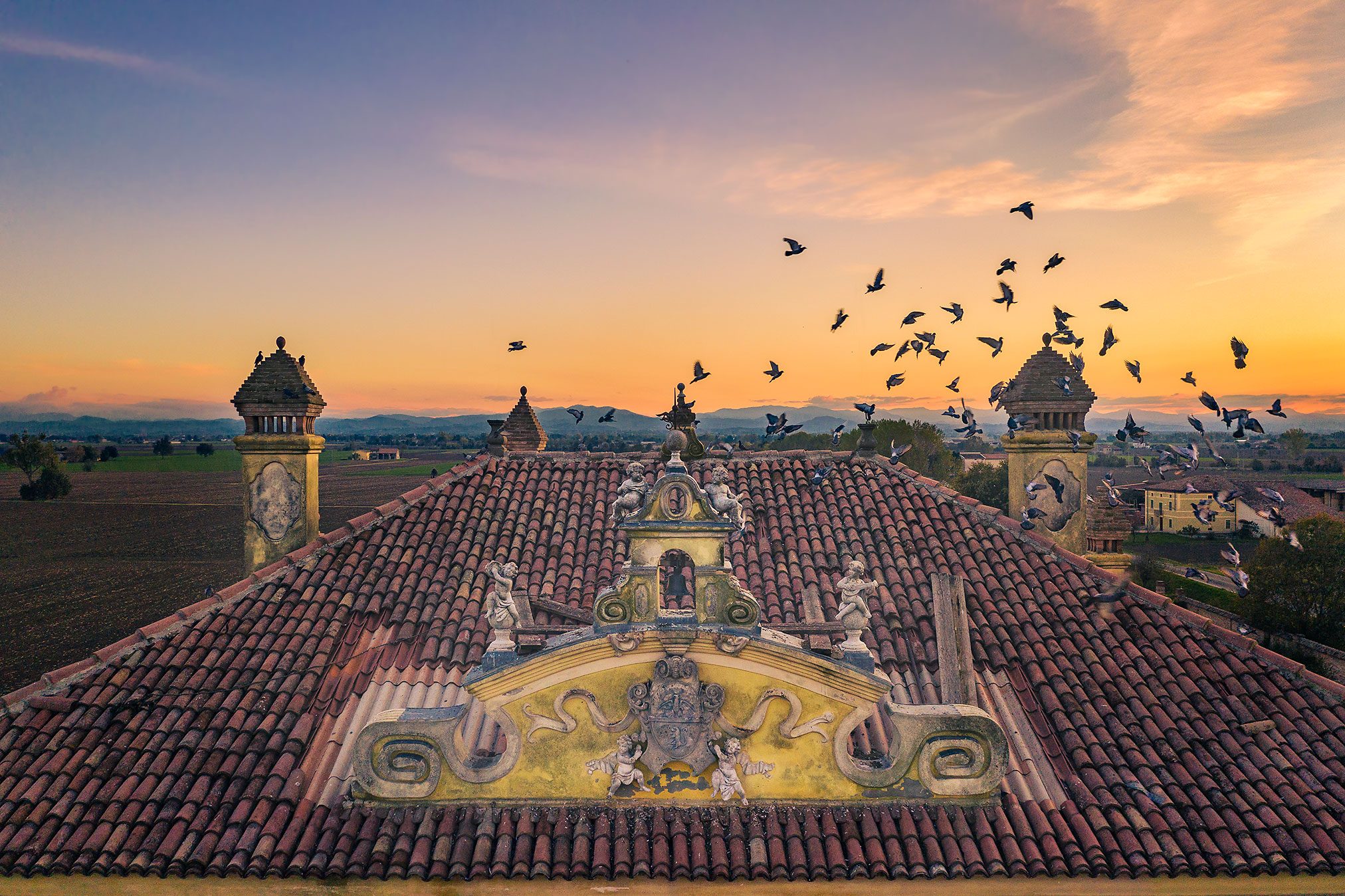 Ornate rooftop pediment of an abandoned villa with a view towards the Alps, Italy