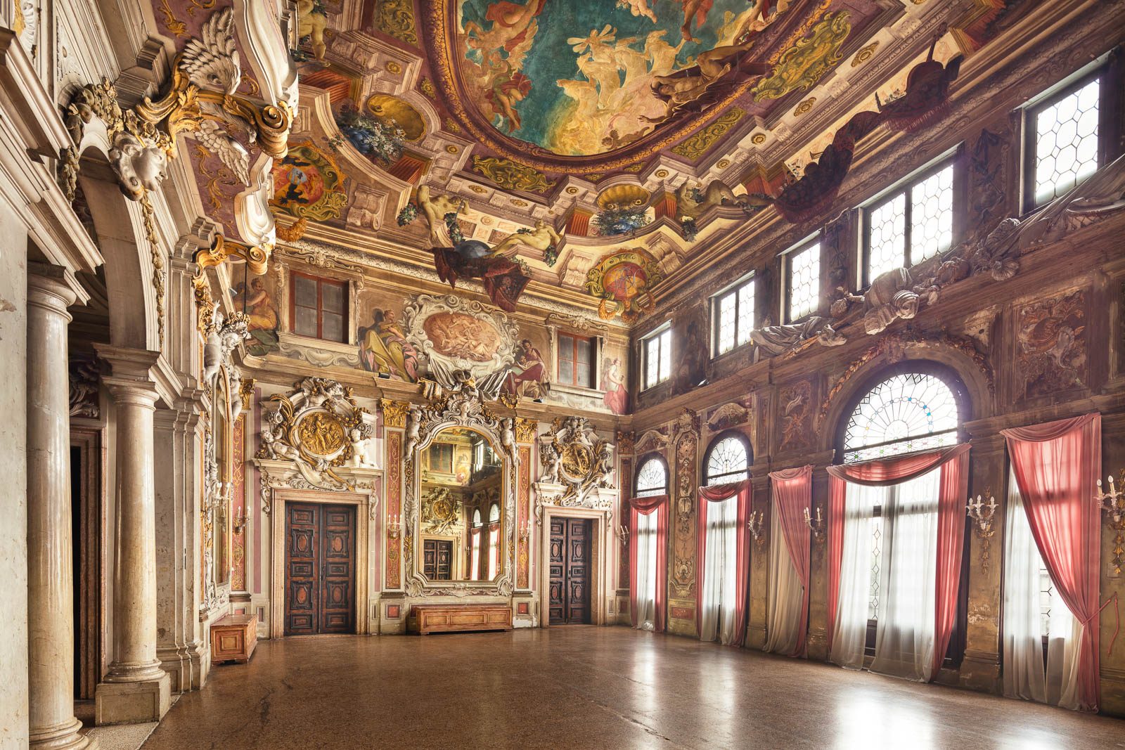 Fresco-decorated ballroom with a mirror and red curtains in Palazzo Zenobio, Venice, Italy