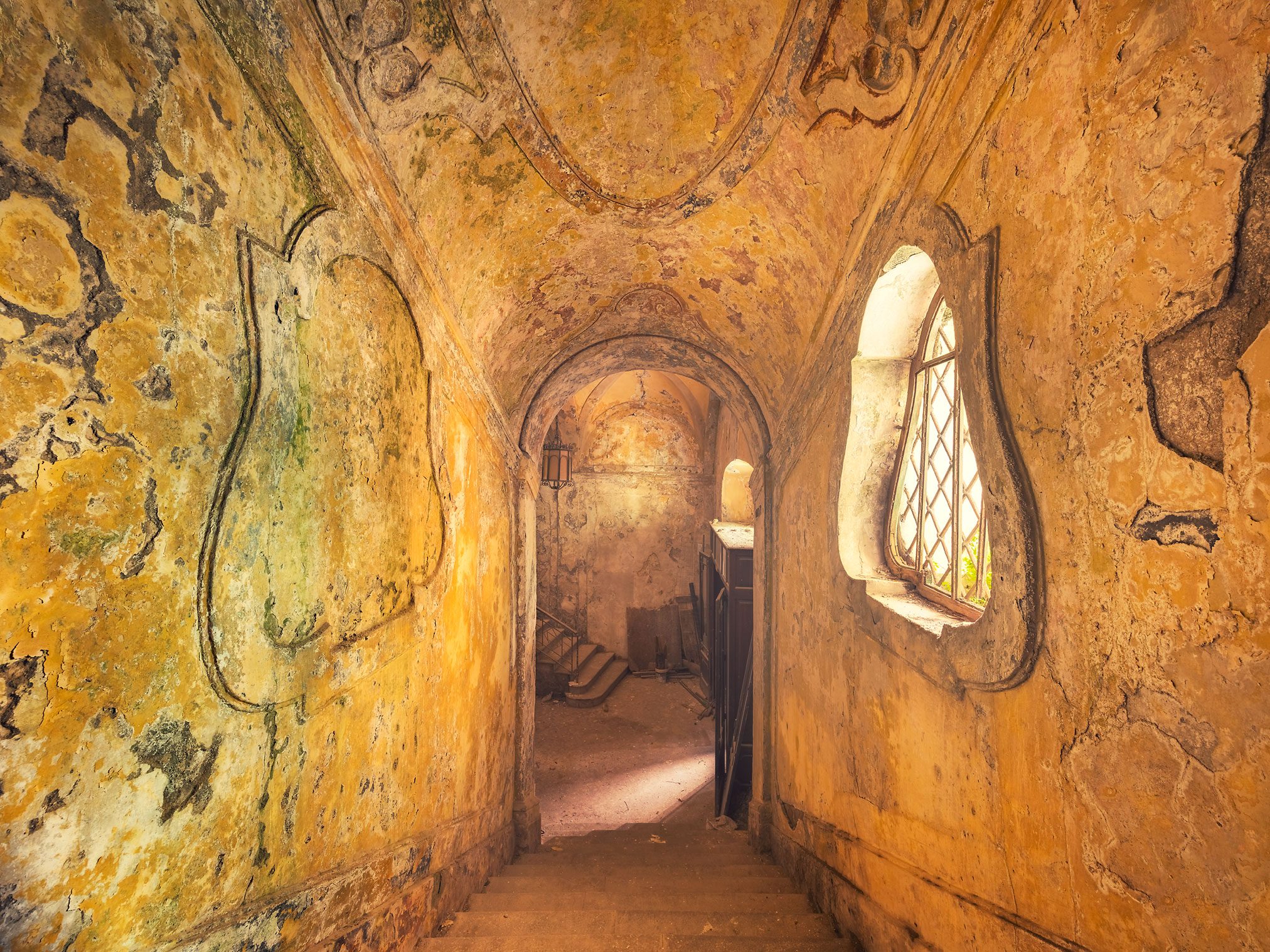 Ochre-toned passage with heraldic reliefs leading to a staircase in a palazzo in Italy