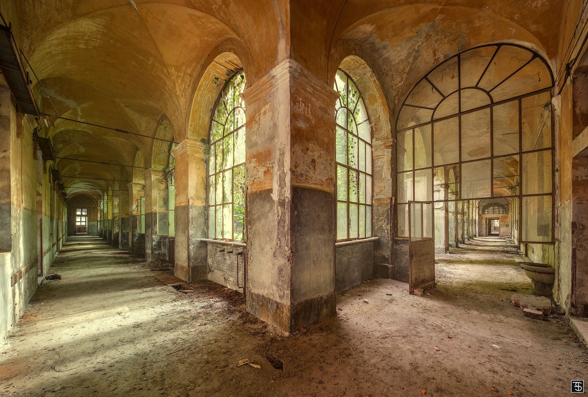 Crossing arcaded corridors in the courtyard of an abandoned psychiatric hospital in Piedmont, Italy