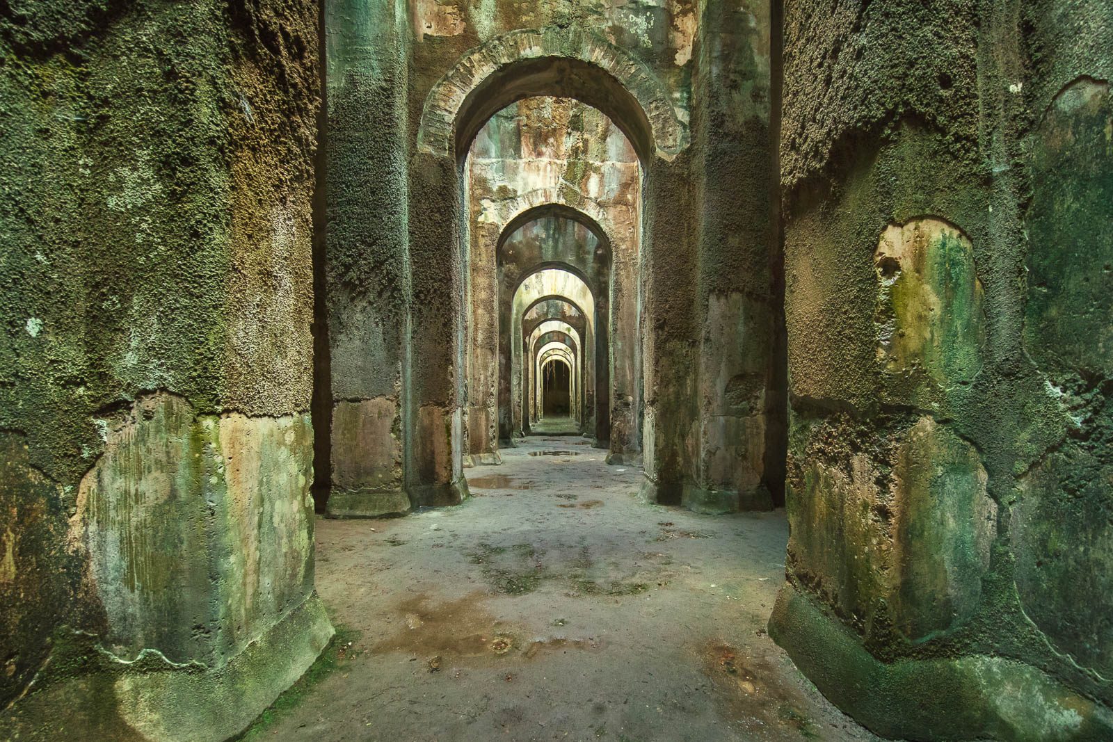 Green moss-covered rows of arches in an underground water reservoir in Calabria, Italy