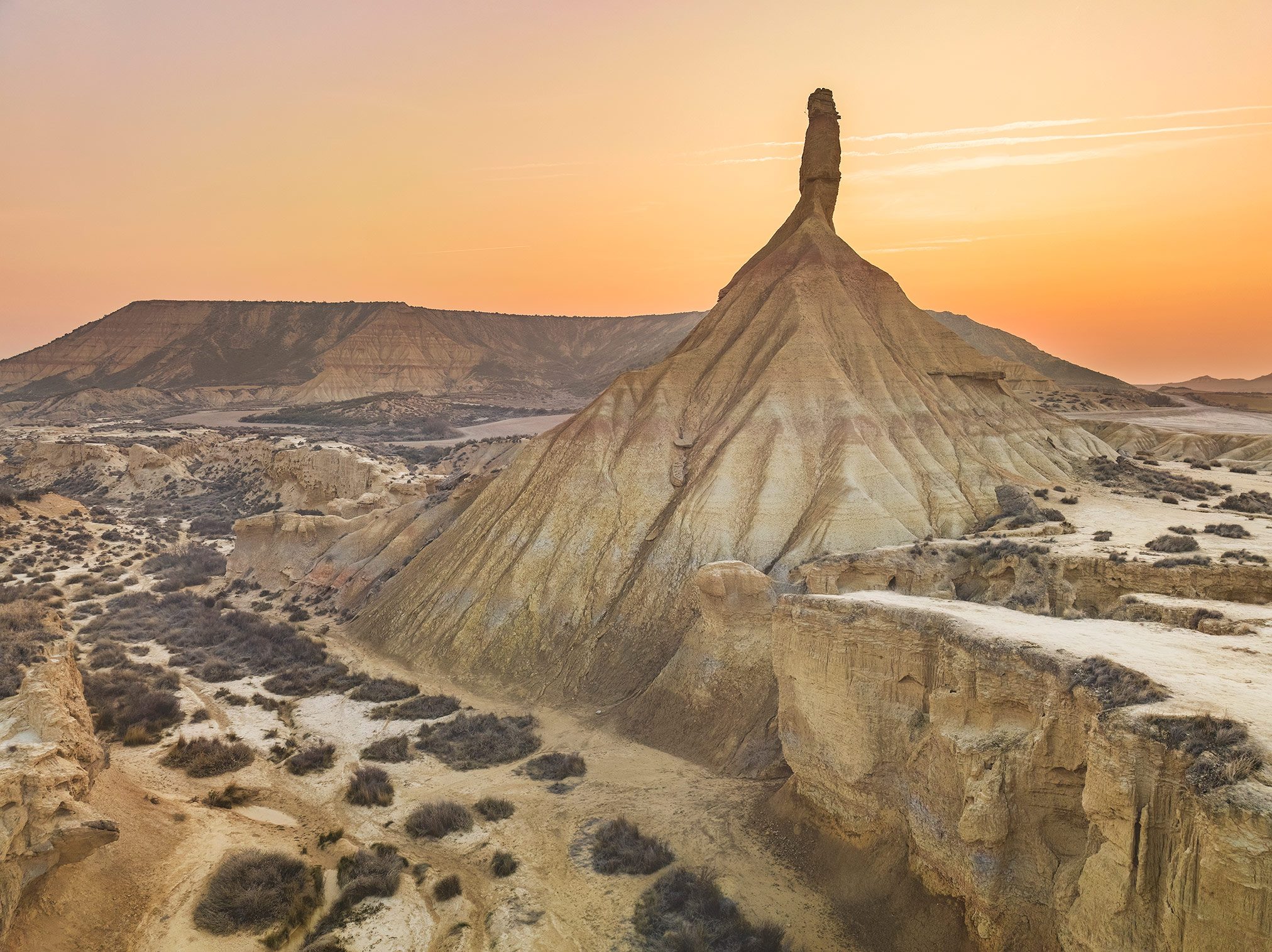 An erosion cone in the Bardenas Reales badlands under an orange evening sky, Spain