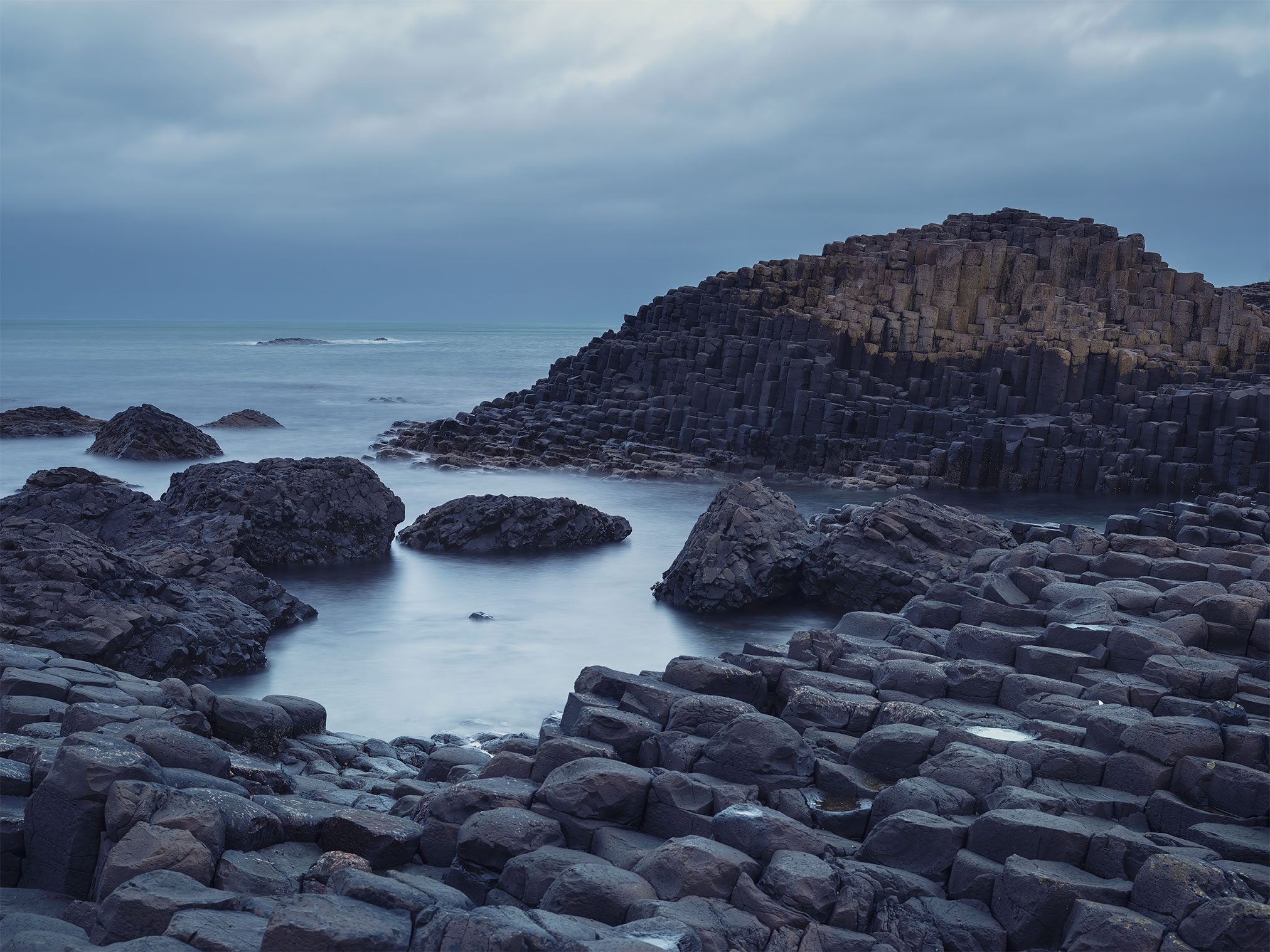 Dark basalt columns in still water under blue dusk light, Northern Ireland