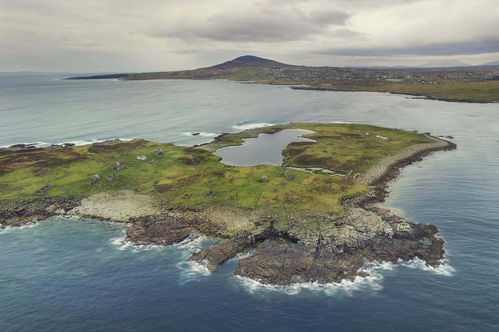 Luftaufnahme einer grünen Insel mit Mauerresten vor der Küste Irlands