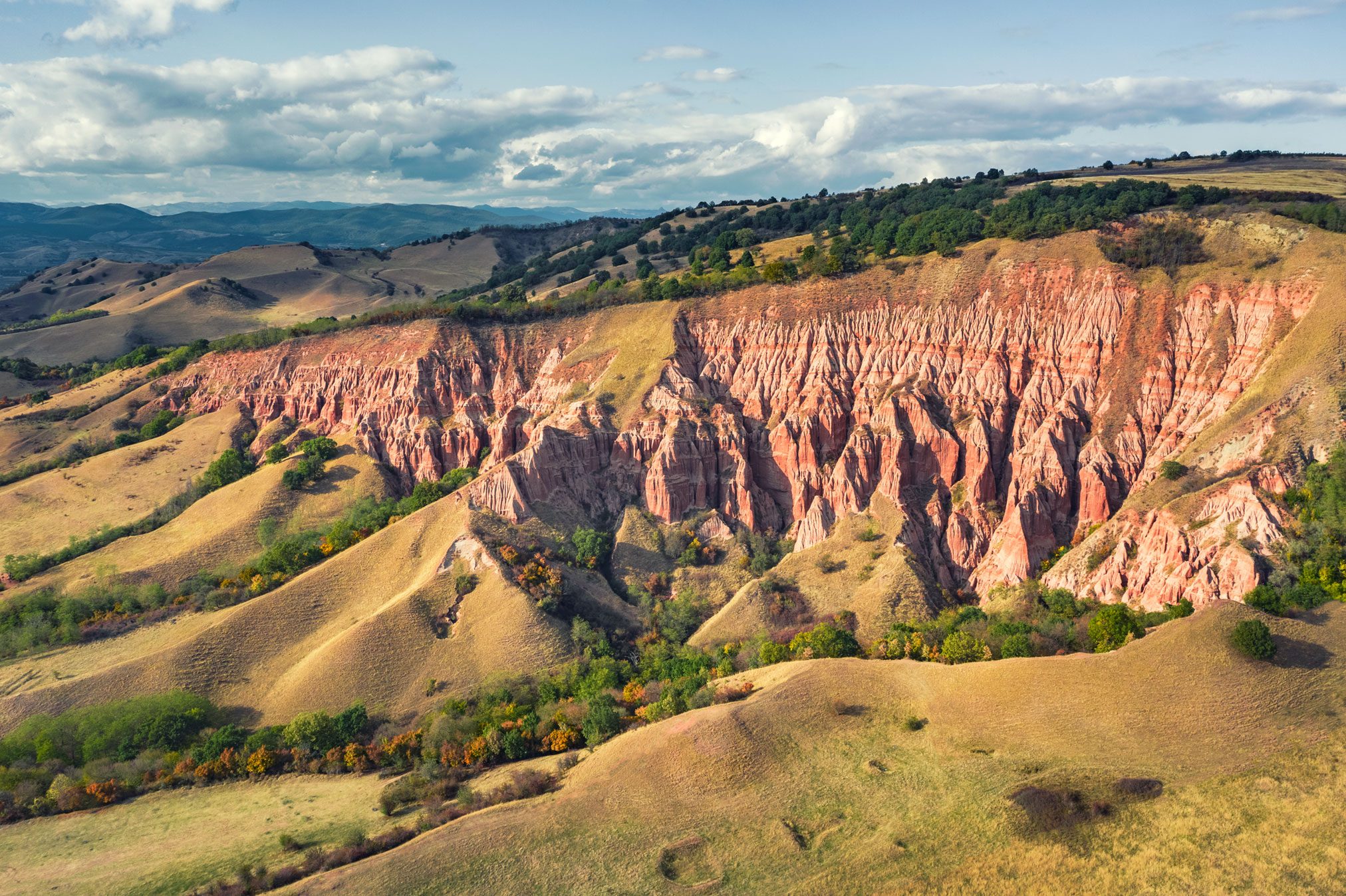 Wide view of the red eroded ravine among green hills in Romania