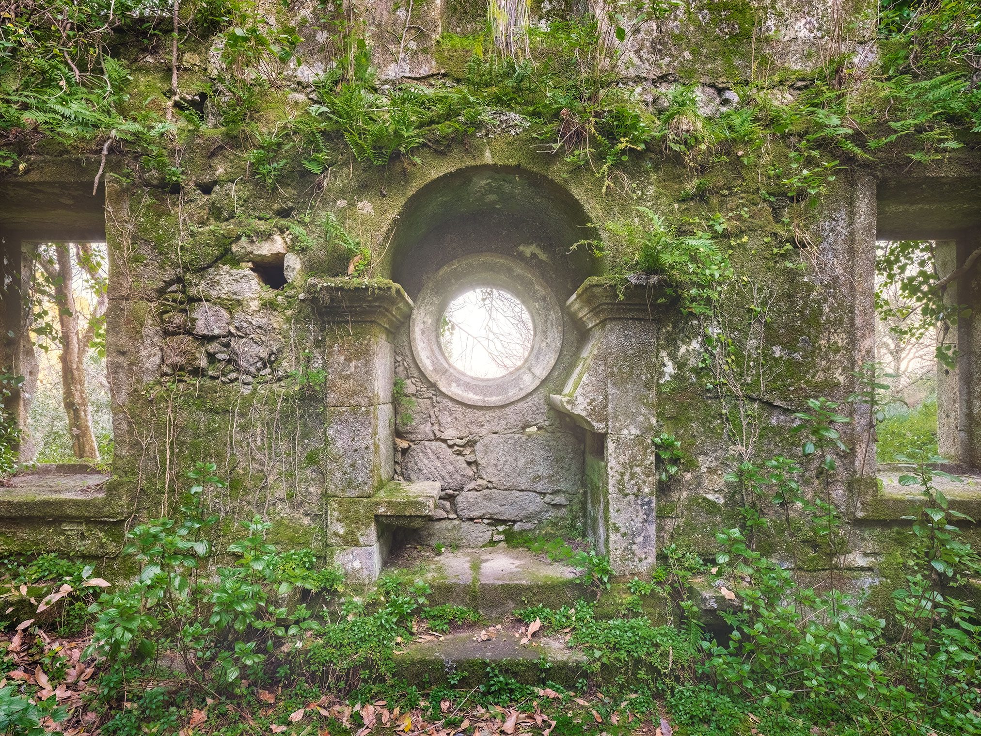 Moss-covered monastery wall with a round window in Portugal