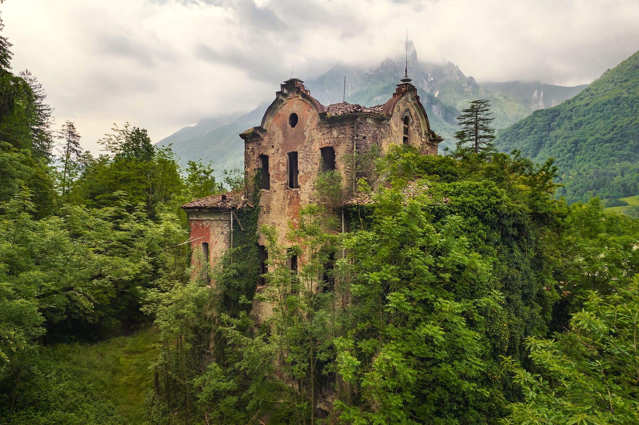 Villa mit zwei Türmen vor bewaldeten Berghängen in Italien