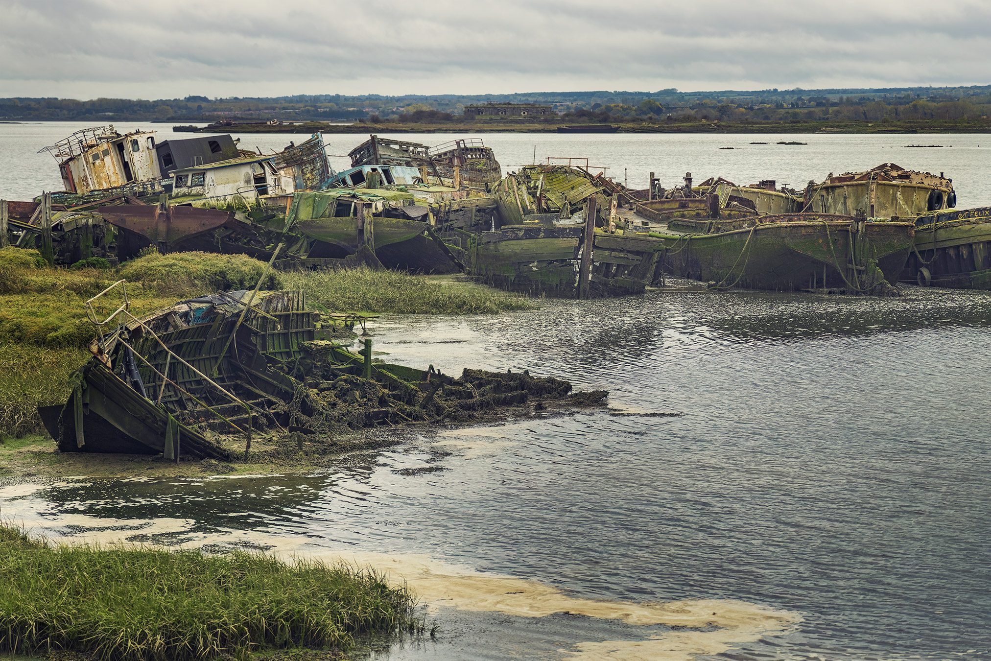 Row of abandoned ship hulls along a tidal shore in England