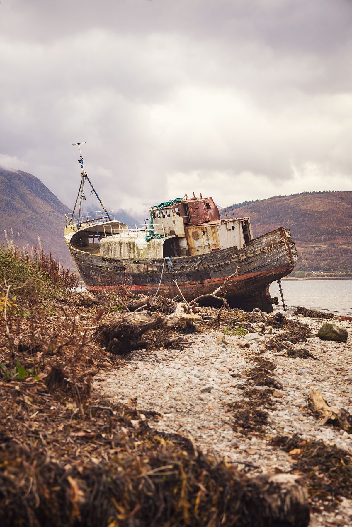Wooden shipwreck with a mast against fog shrouded mountains in Scotland
