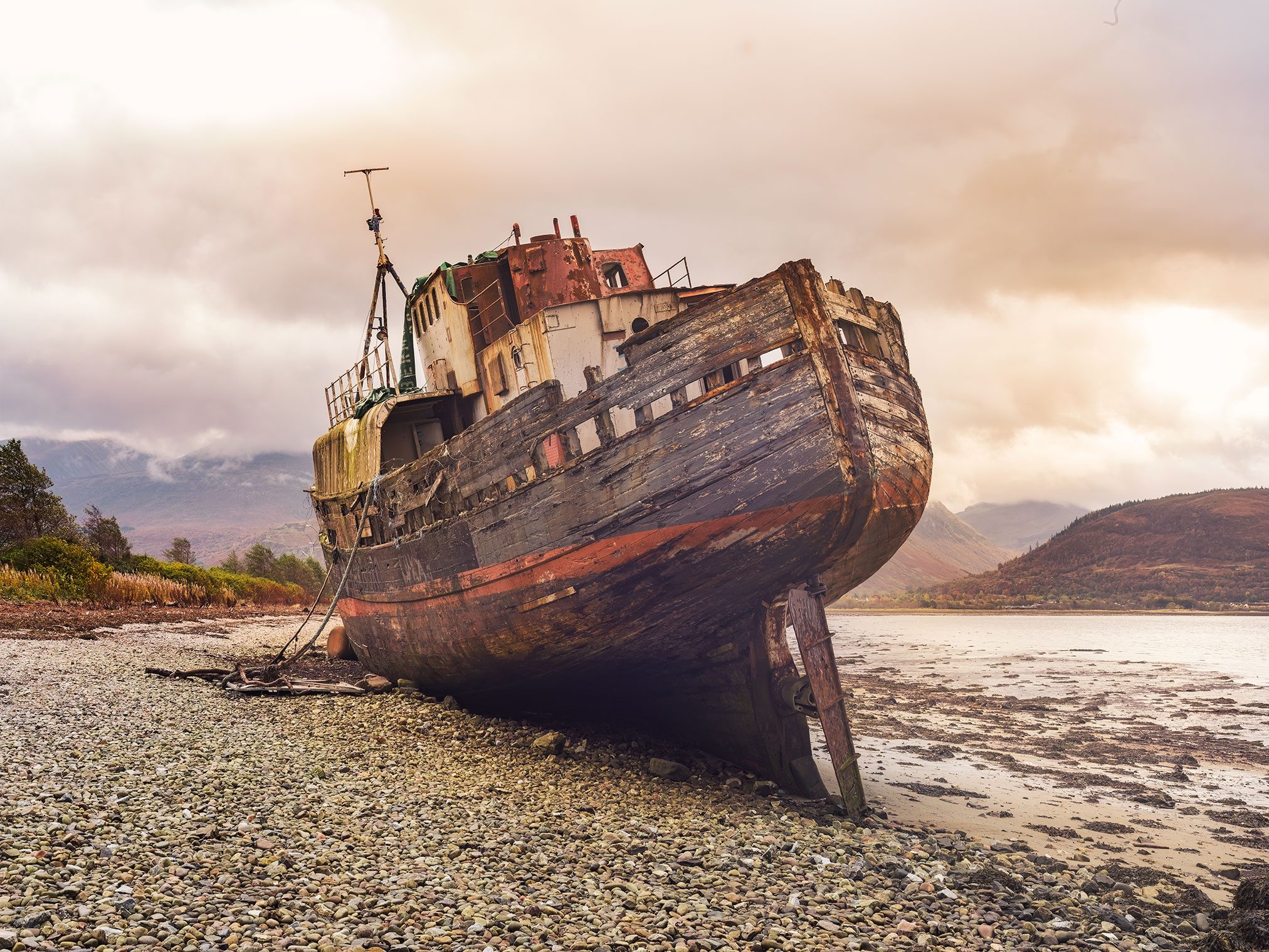 Hölzernes Schiffswrack an einem Kiesstrand vor Berglandschaft in Schottland