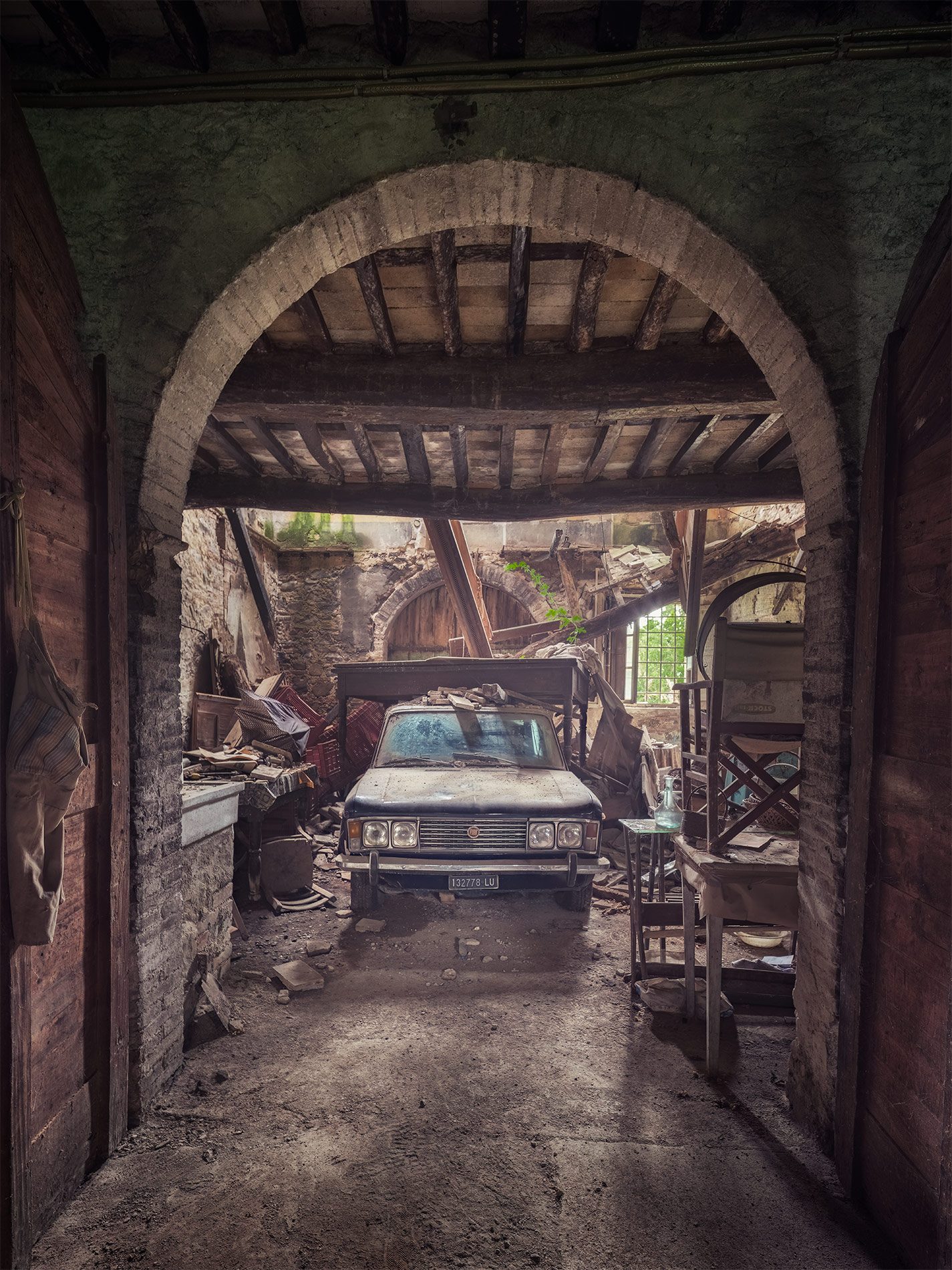 Old Fiat sedan beneath a collapsed roof in an abandoned barn in Italy