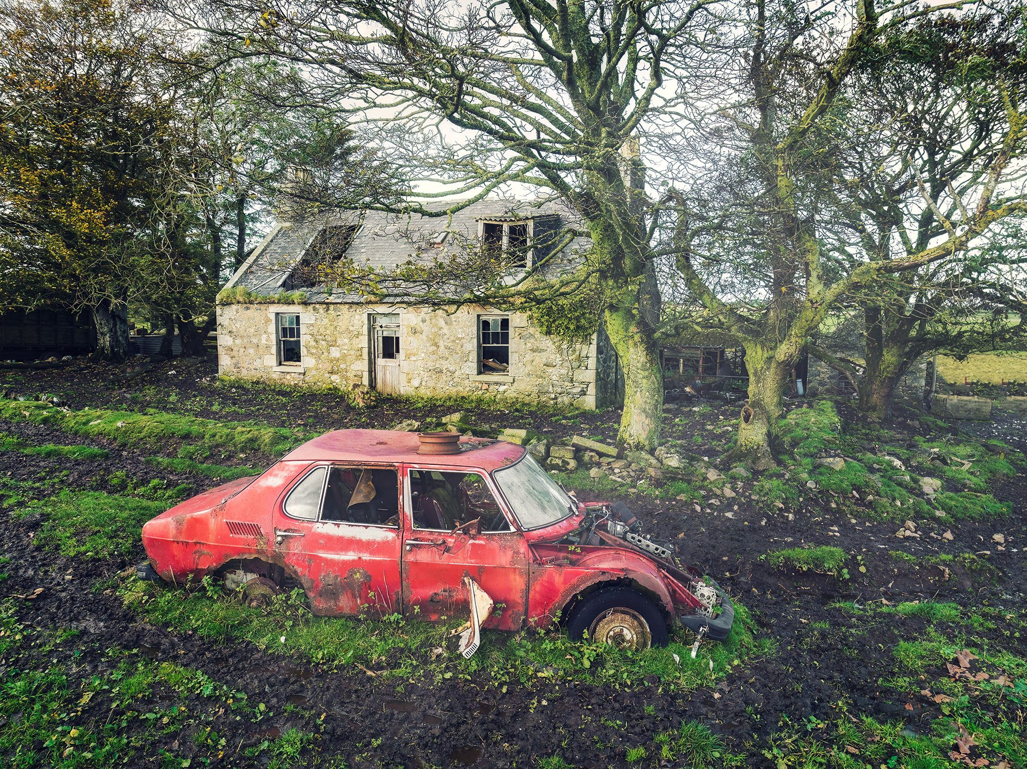 Rotes Autowrack vor einem verlassenen Steinhaus in den Highlands, Schottland