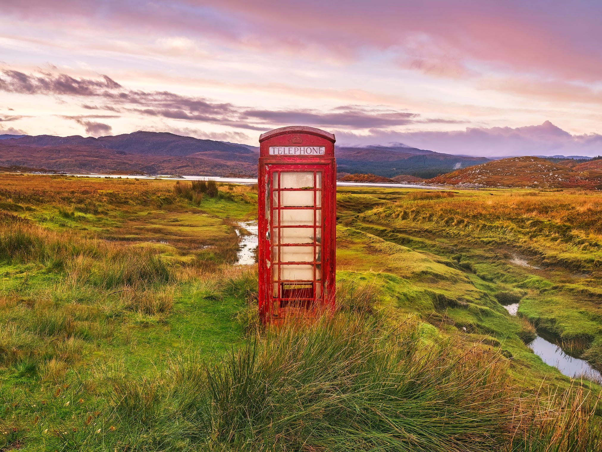 Red telephone box beside a loch in a moorland in Scotland