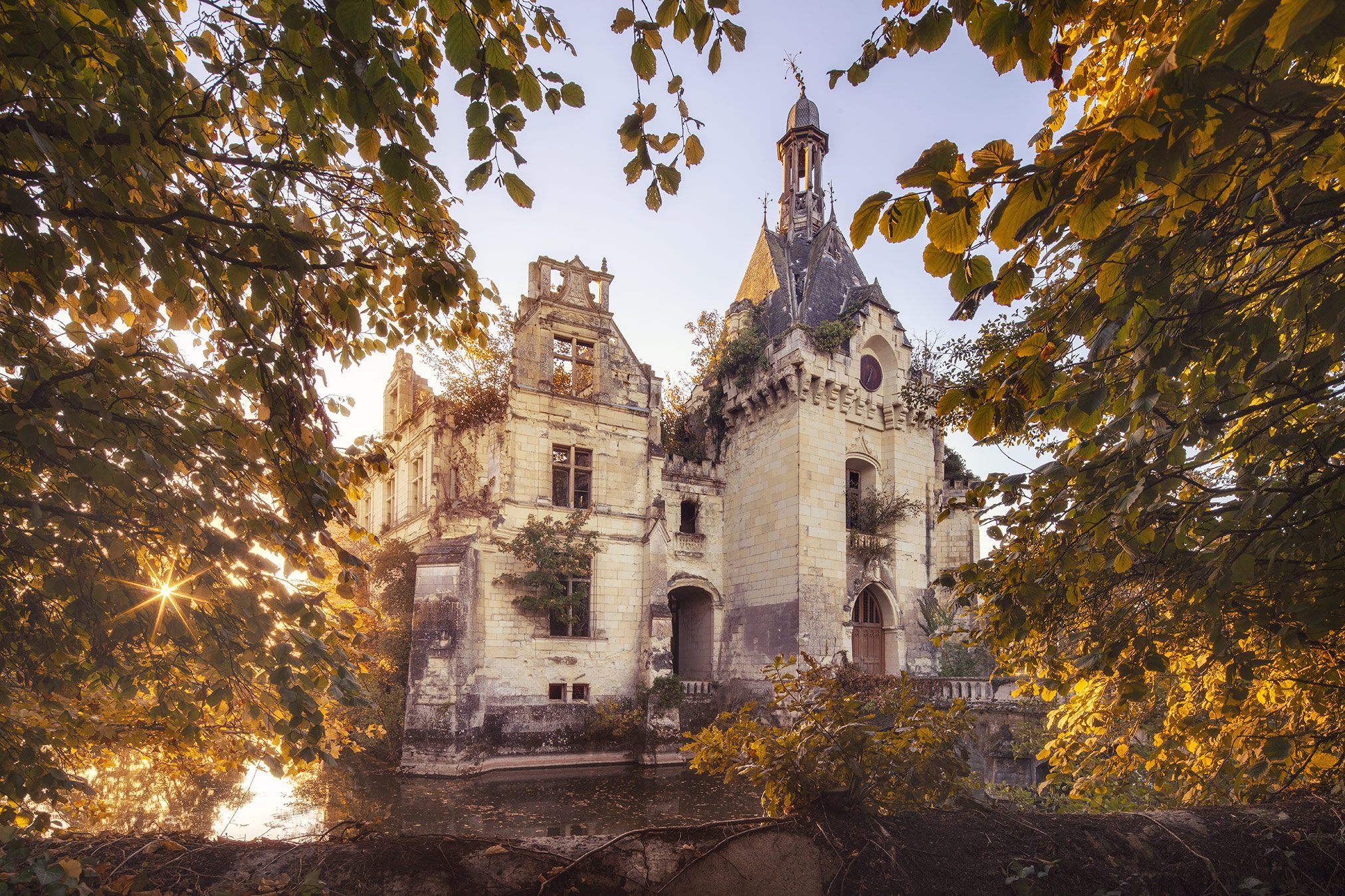 Ruined moated chateau with a tower, framed by autumn foliage in France