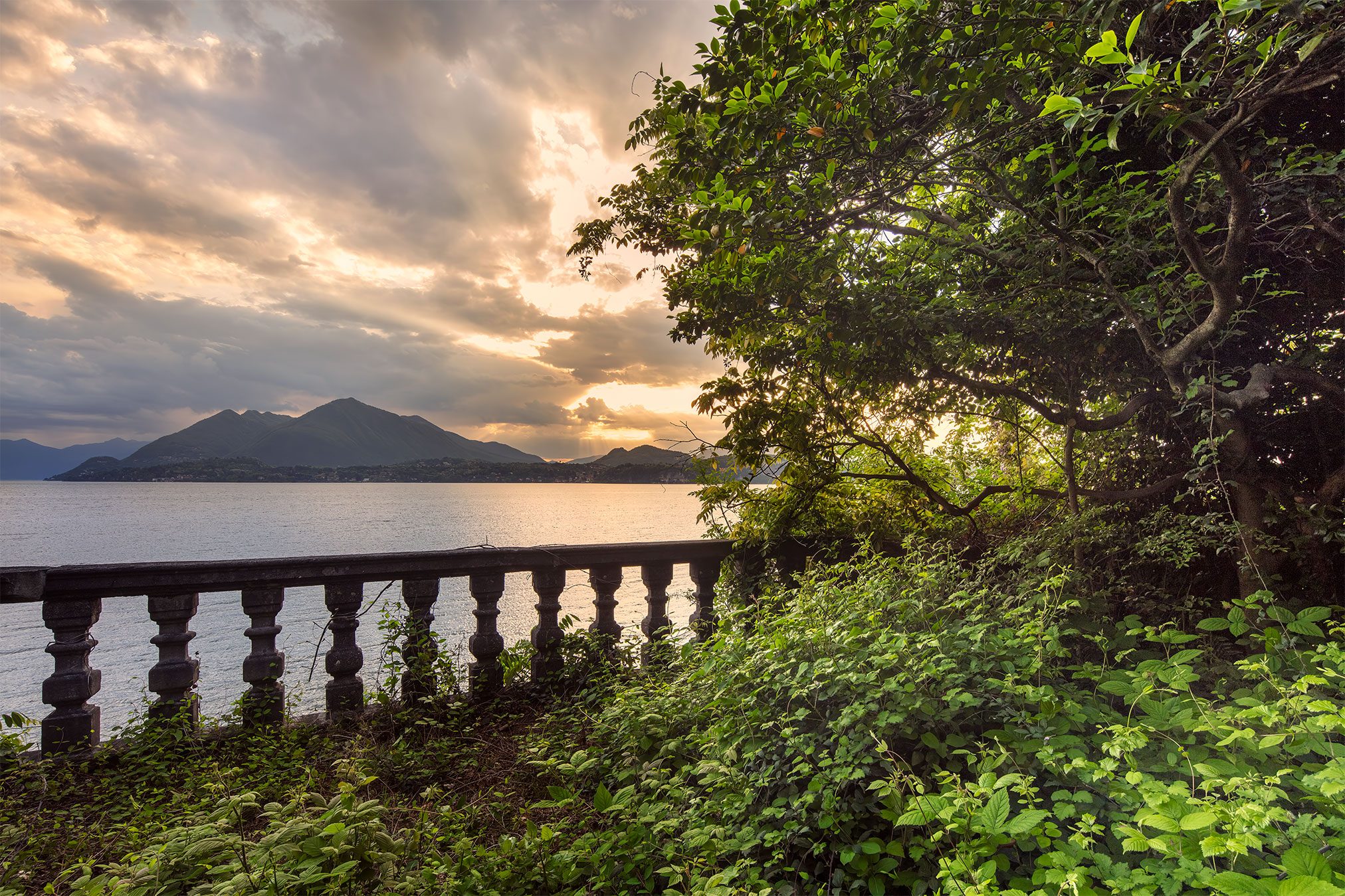 Stone balustrade beneath trees overlooking a lake in Italy