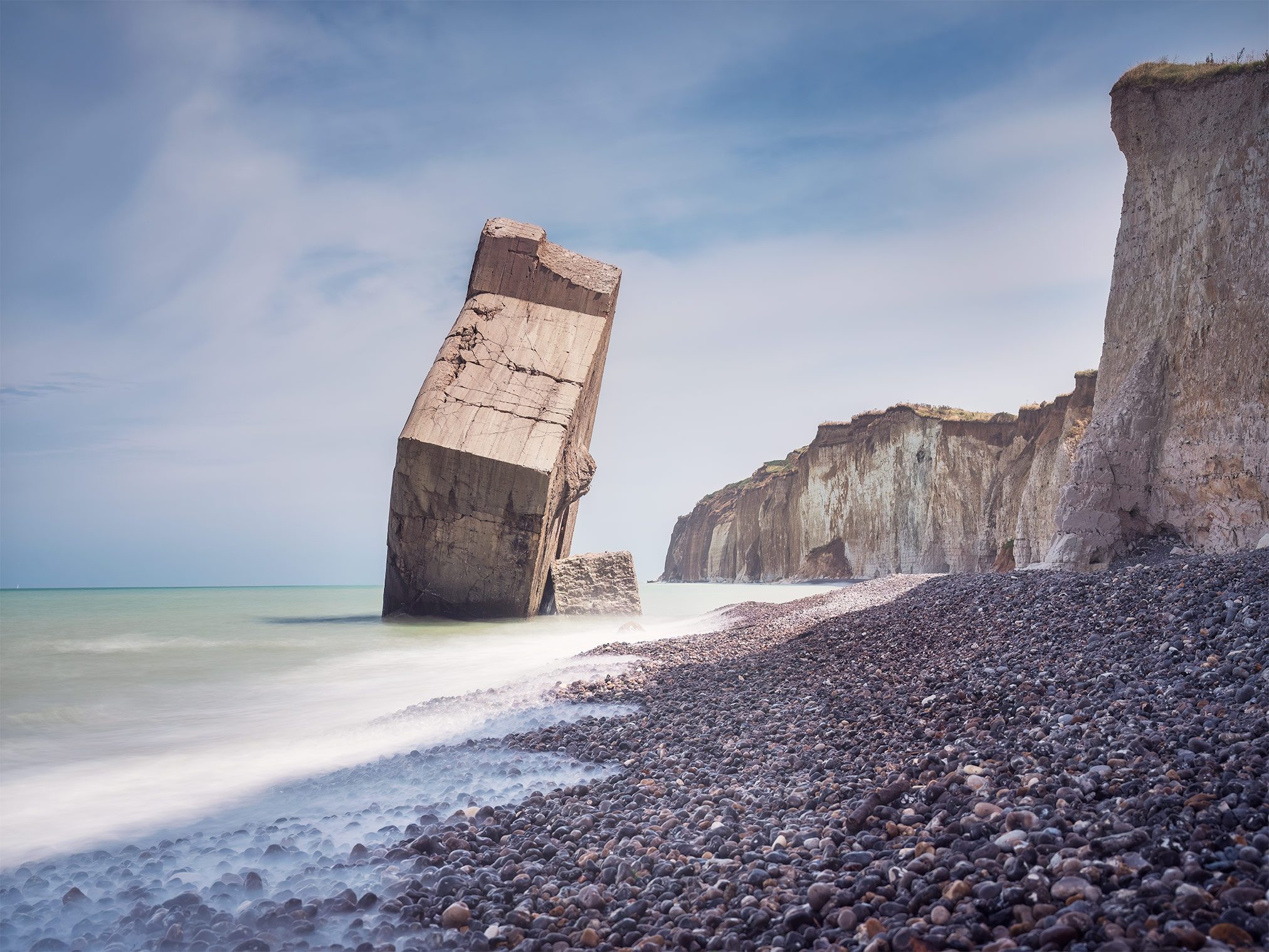 Toppled bunker on a pebble beach beneath chalk cliffs in France