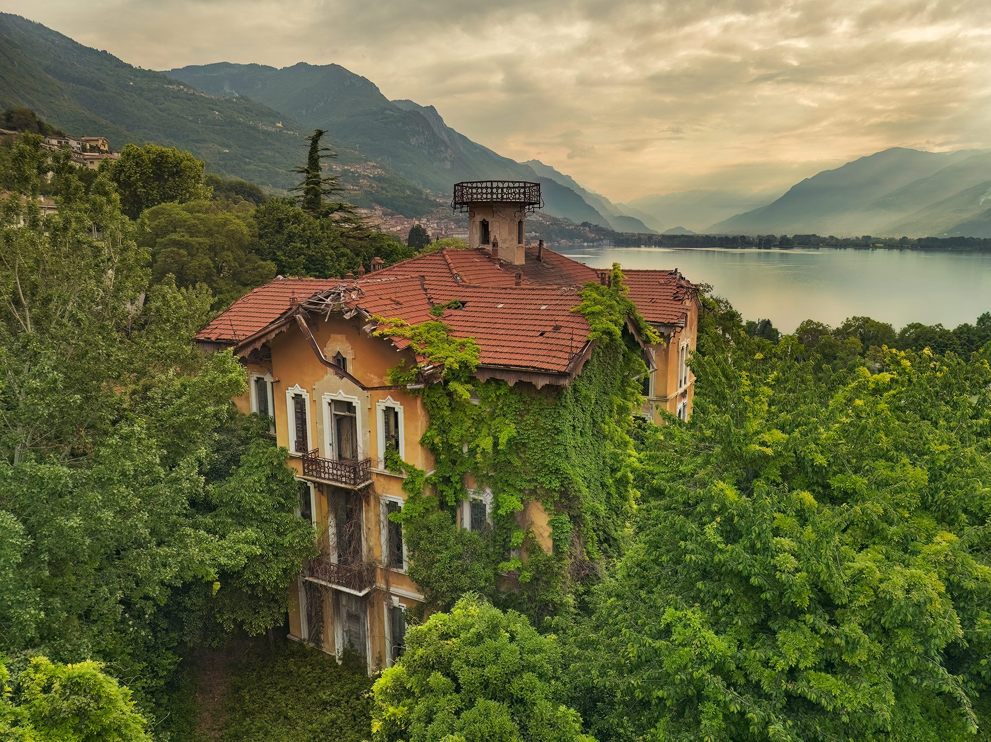 Villa with a red tiled roof above a lake in morning mist, Italy