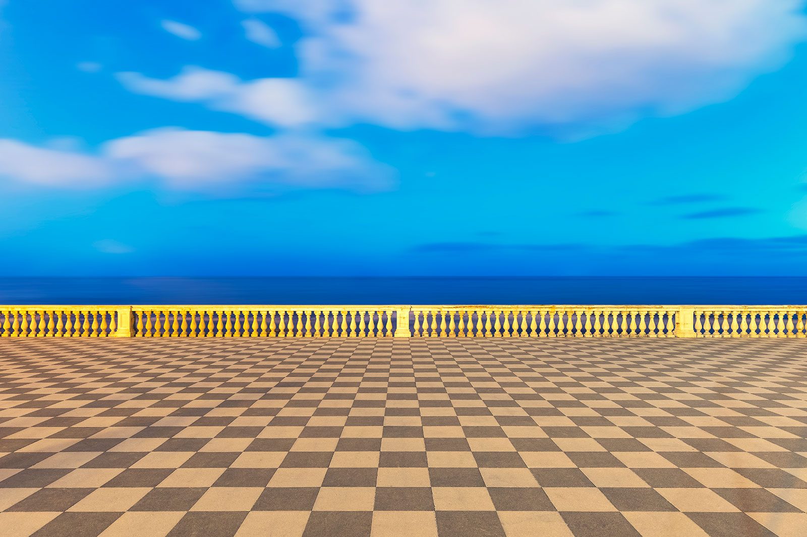 Empty square with a chequered tile pattern under a blue sky, Italy