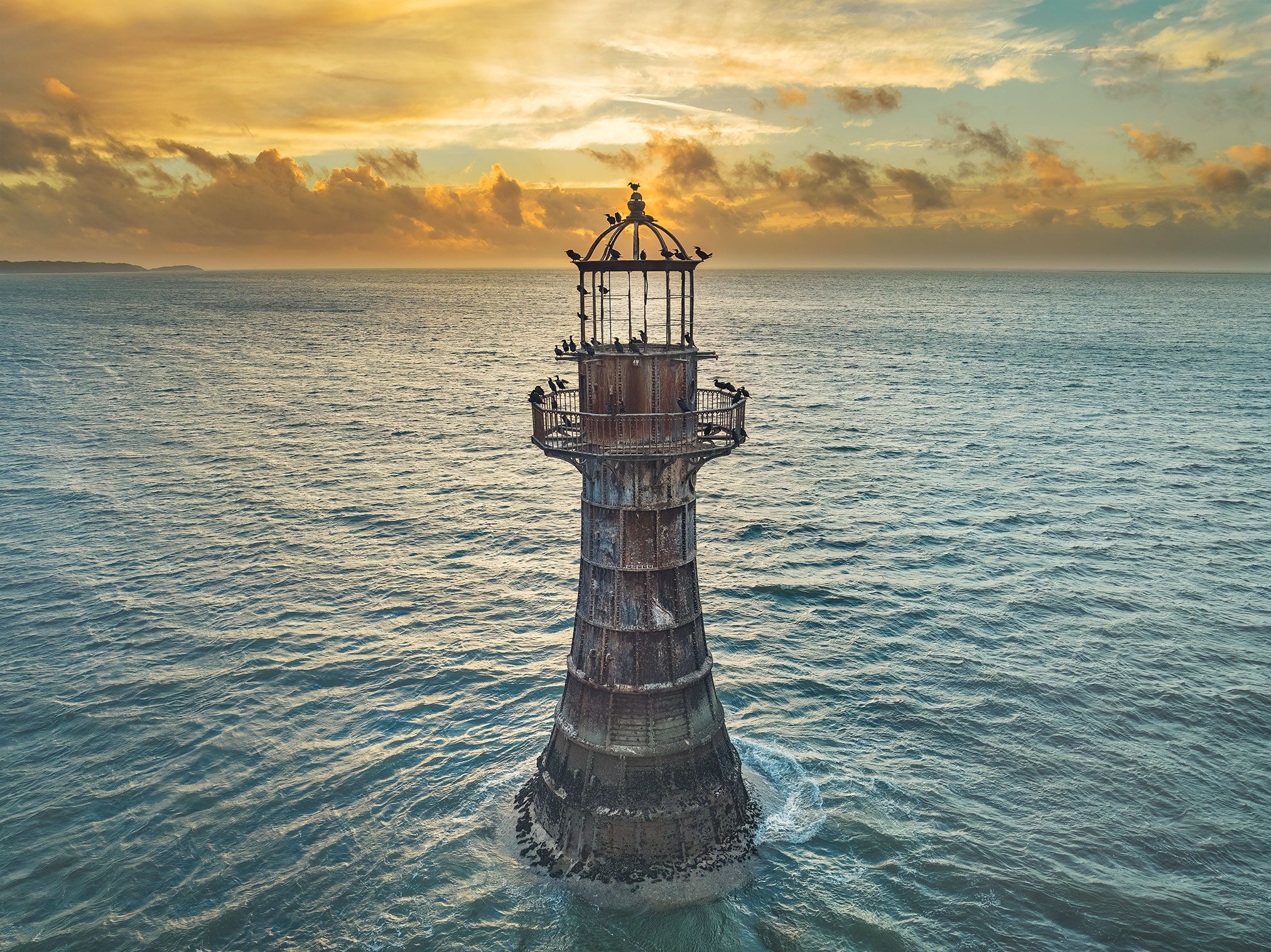 Cast iron lighthouse in the sea with resting birds at sunset, Wales