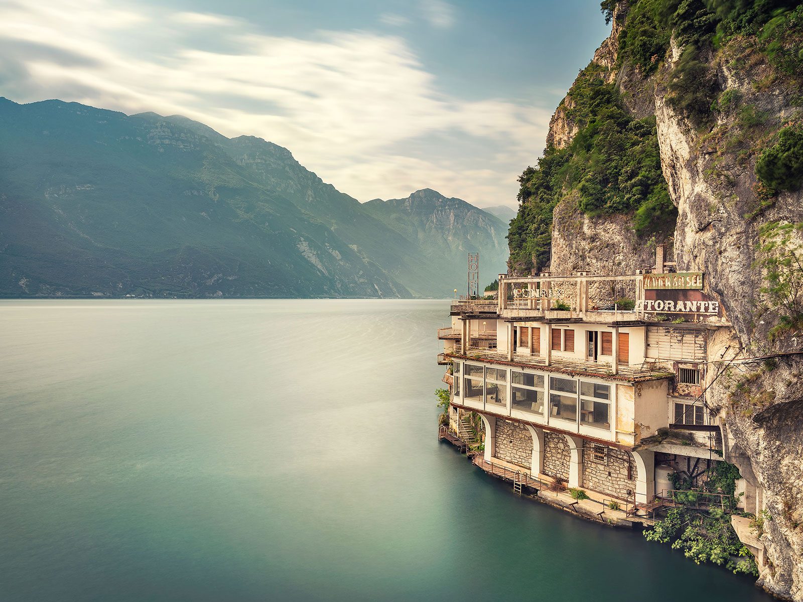 Abandoned hotel on a cliff face above a lake in Italy