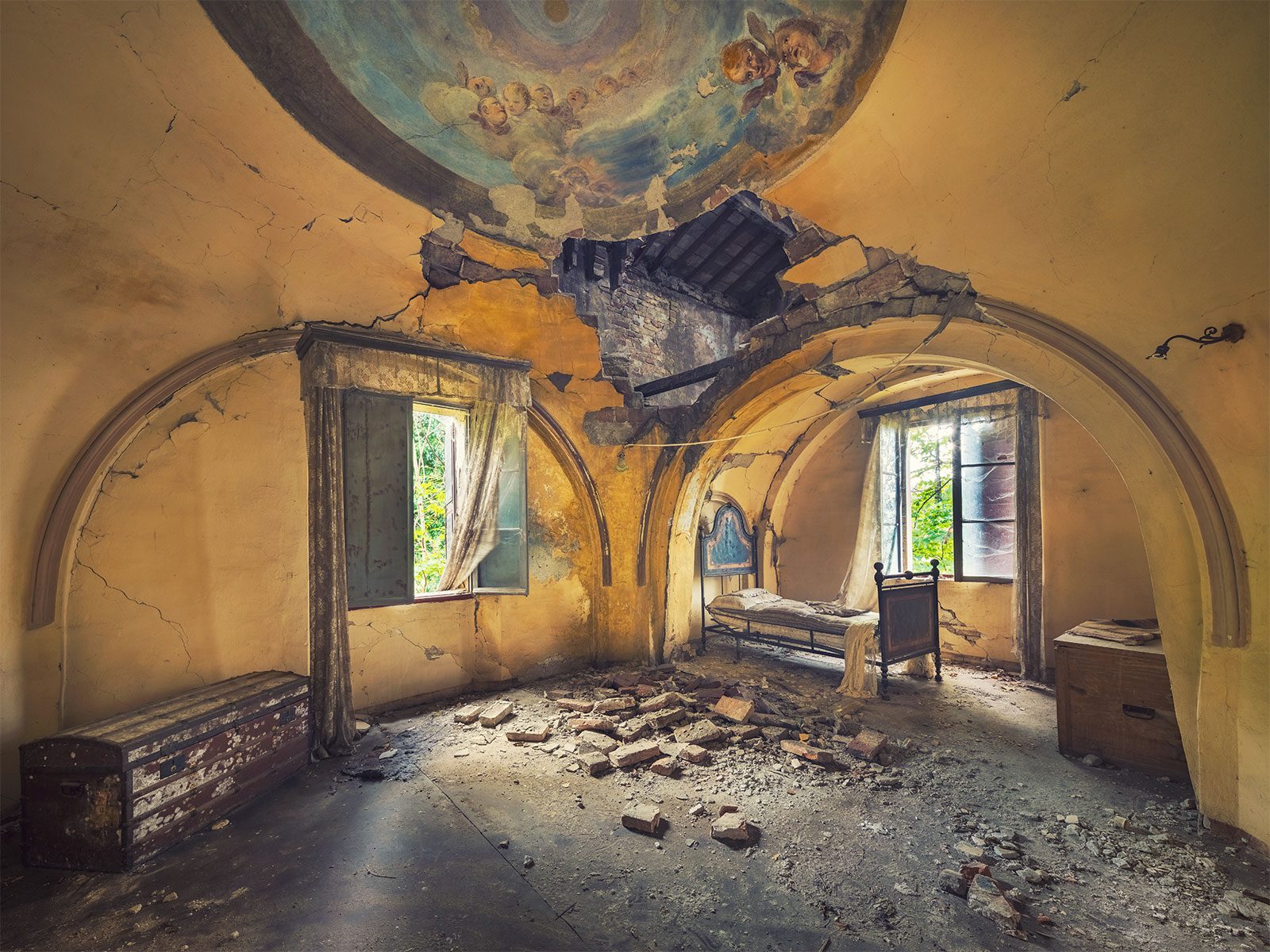 Iron bed beneath a collapsed domed ceiling in a rural villa in Italy