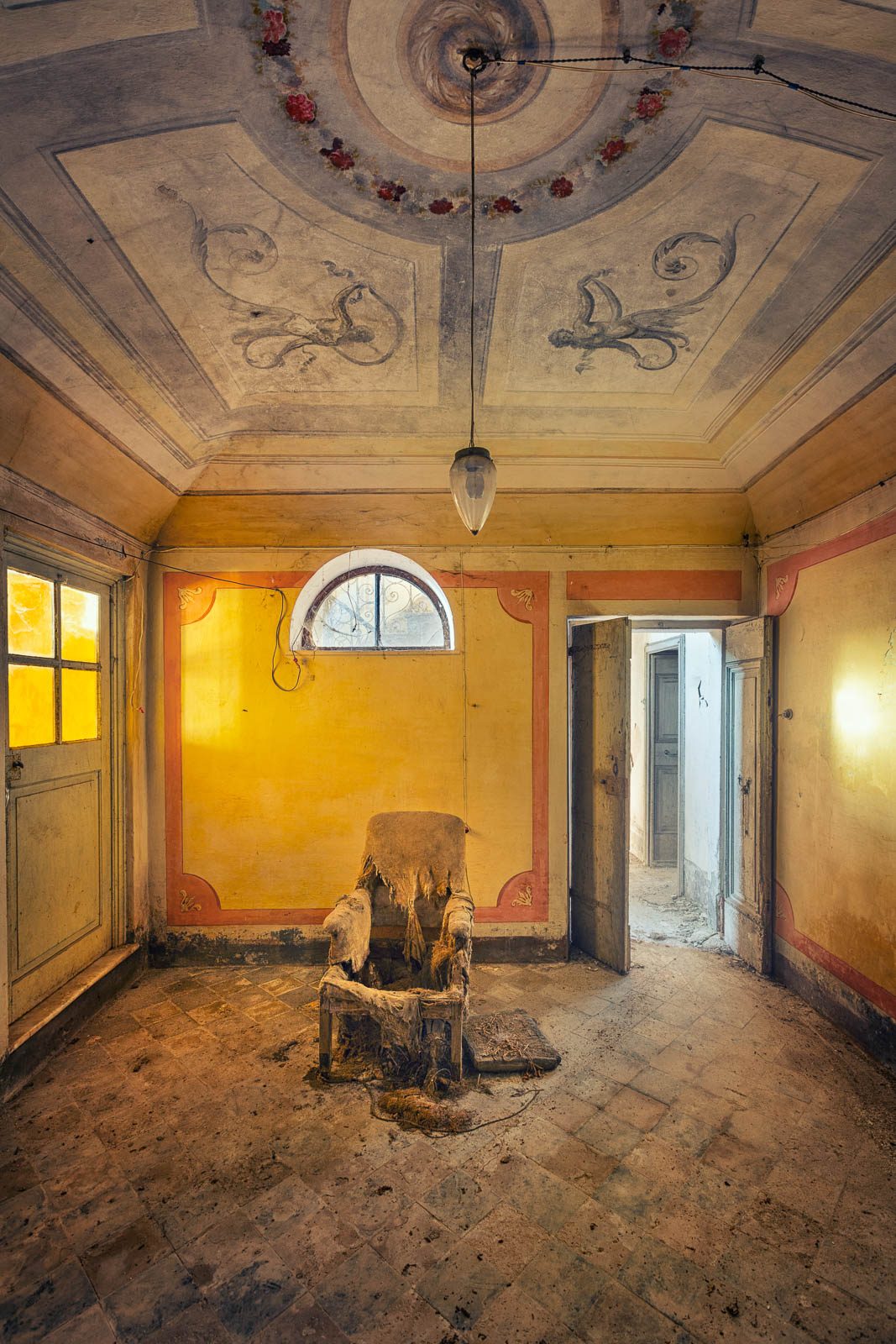 Old armchair beneath a painted ceiling rosette in a forgotten villa in Tuscany
