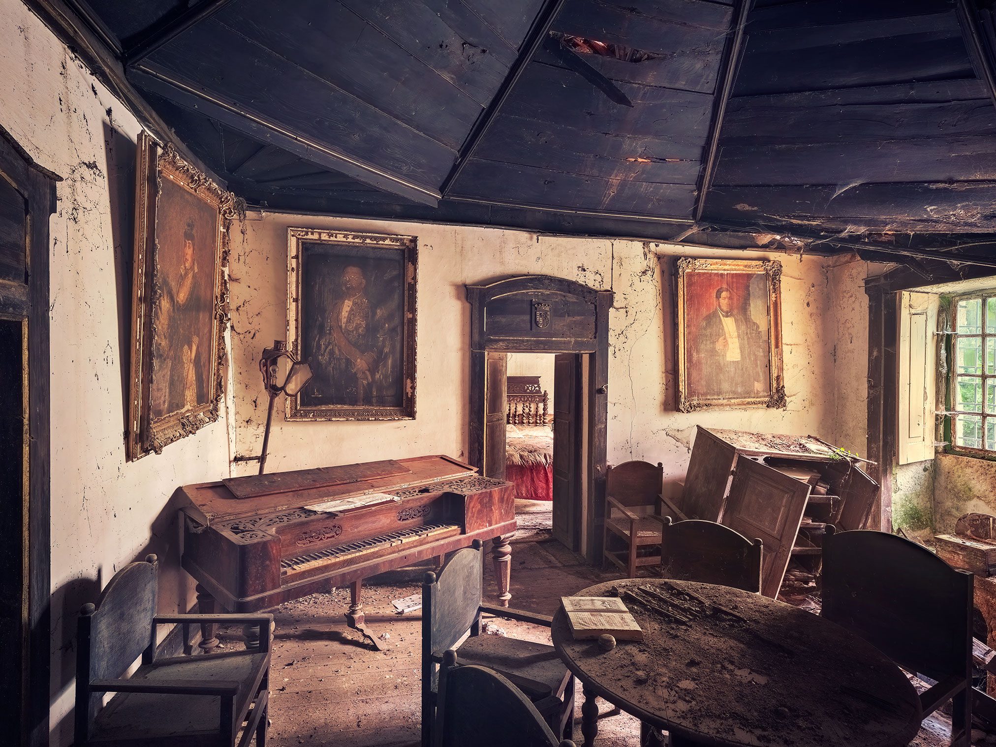 Room with portrait paintings and an old piano in a villa abandoned for decades in Portugal