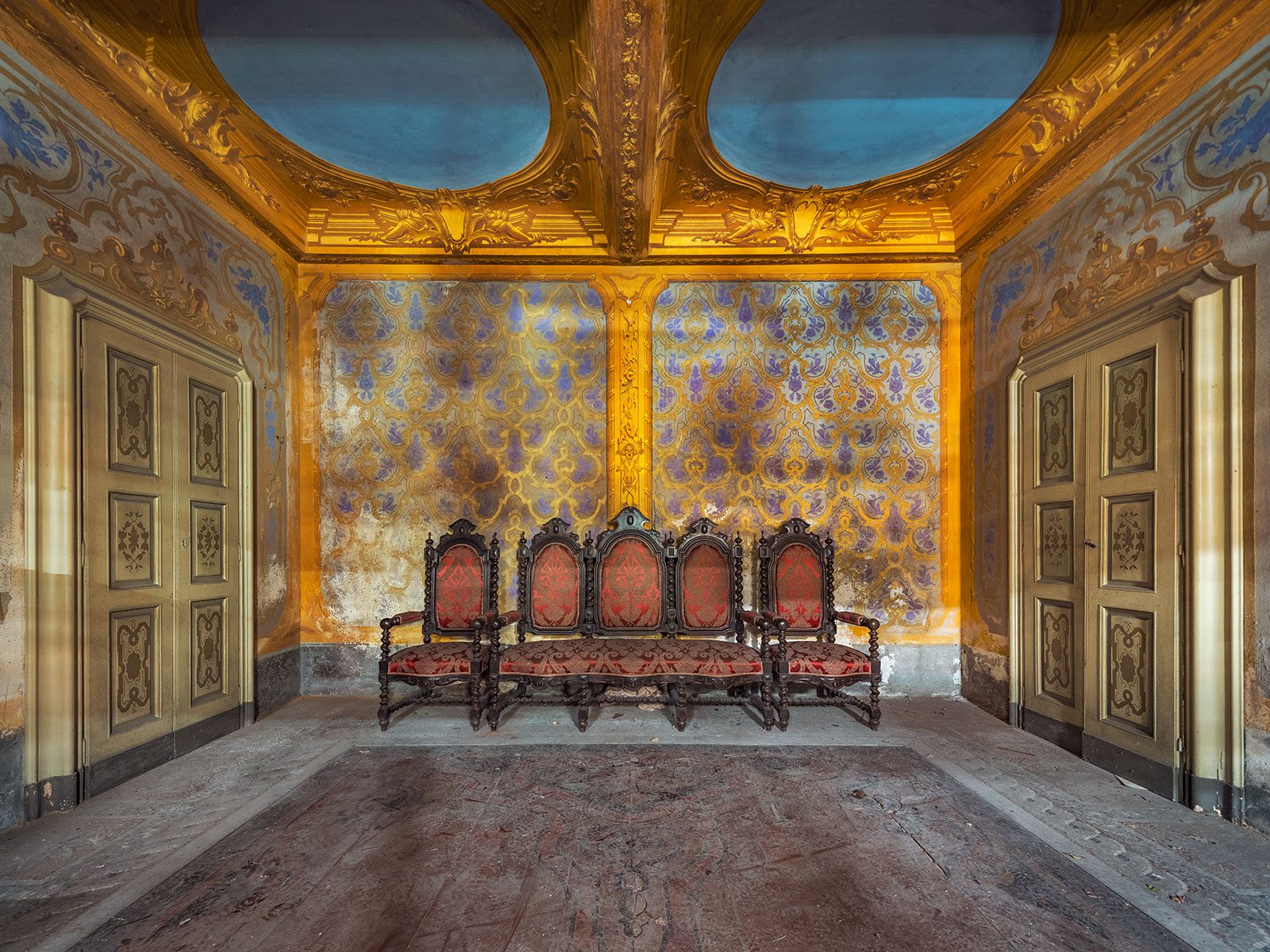 Vergoldeter Saal mit roten Stühlen in einem verlassenen Palazzo in Italien