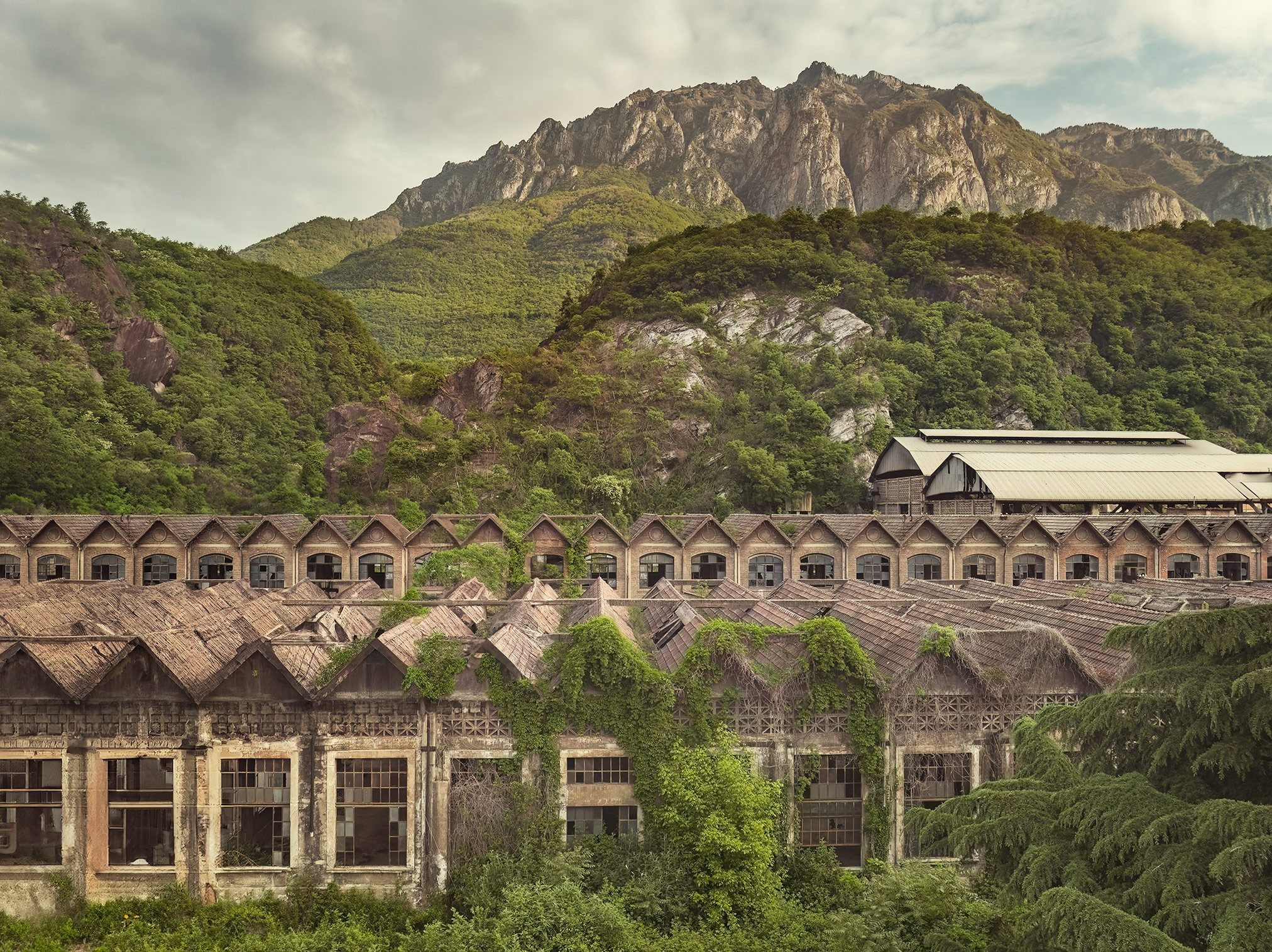 Wide view of a factory building before a jagged mountain range in Italy