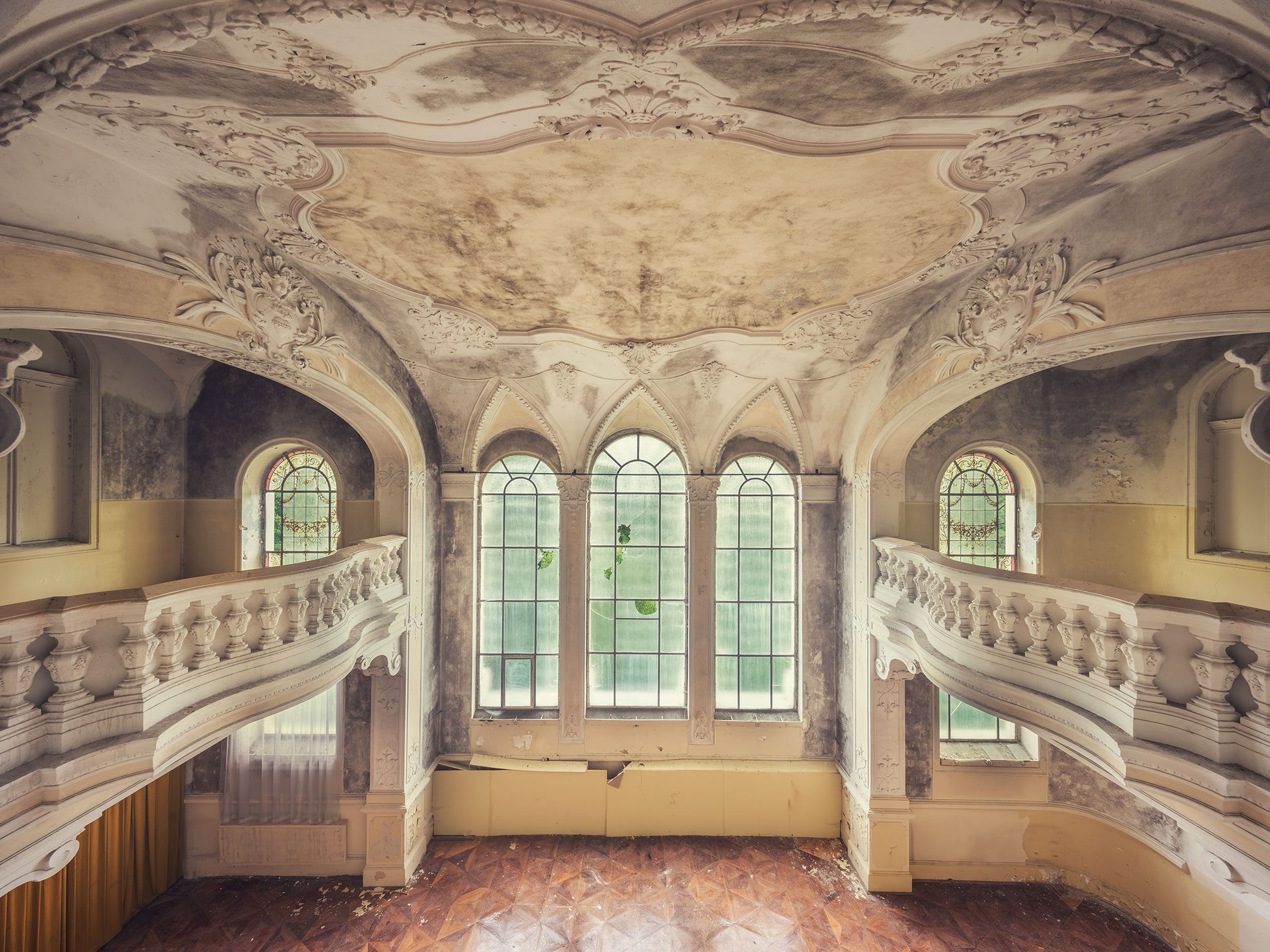 Main hall with curved staircases and a rococo stucco ceiling in an abandoned castle in the Czech Republic