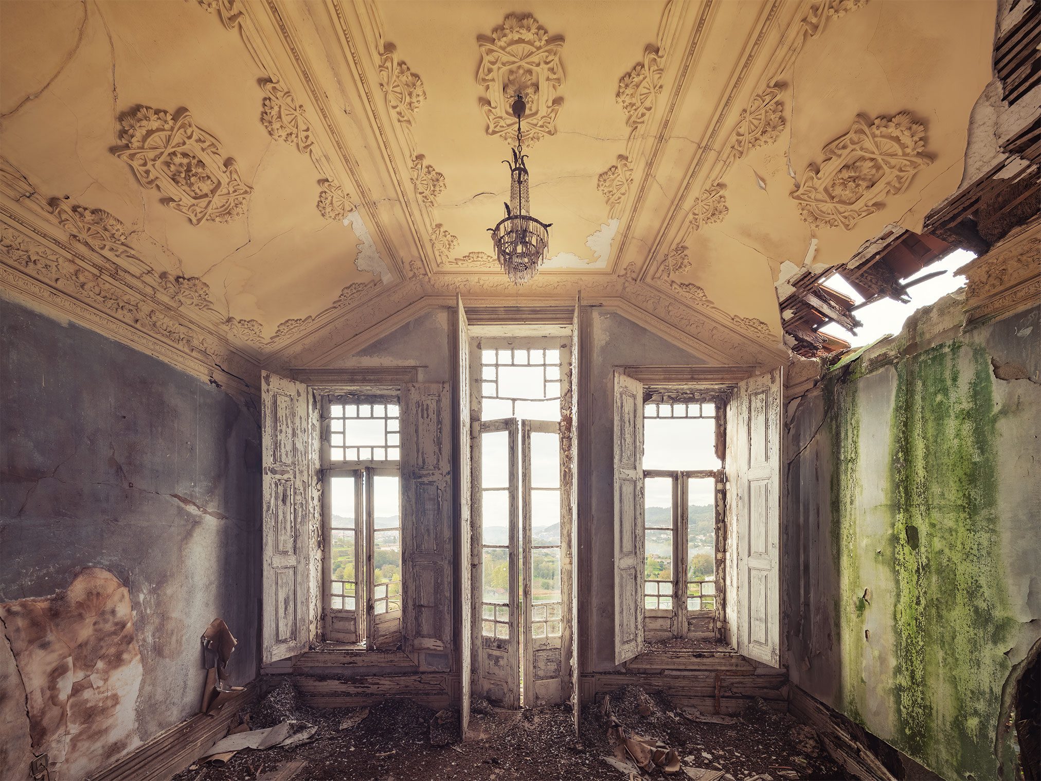 Room with a stucco ceiling, chandelier and hill view in a derelict Art Nouveau villa in Portugal