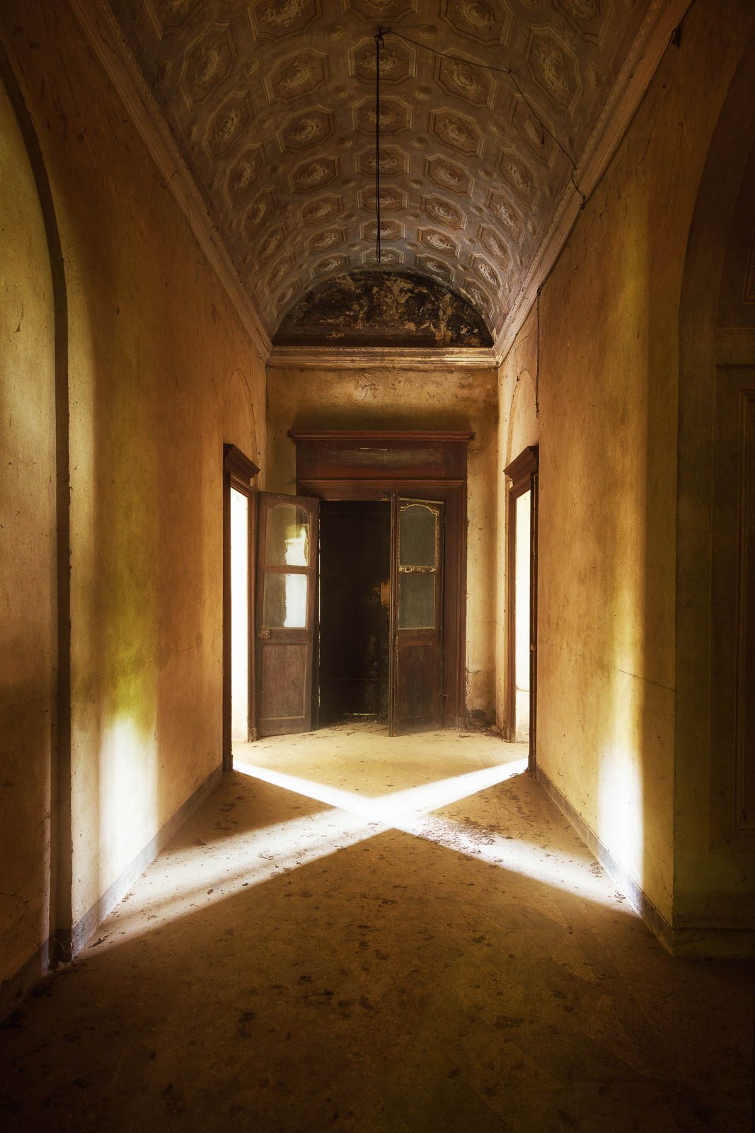 Gewölbter Flur mit kreuzförmigem Lichteinfall aus zwei offenen Türen in einem verlassenen Palazzo, Piemont, Italien