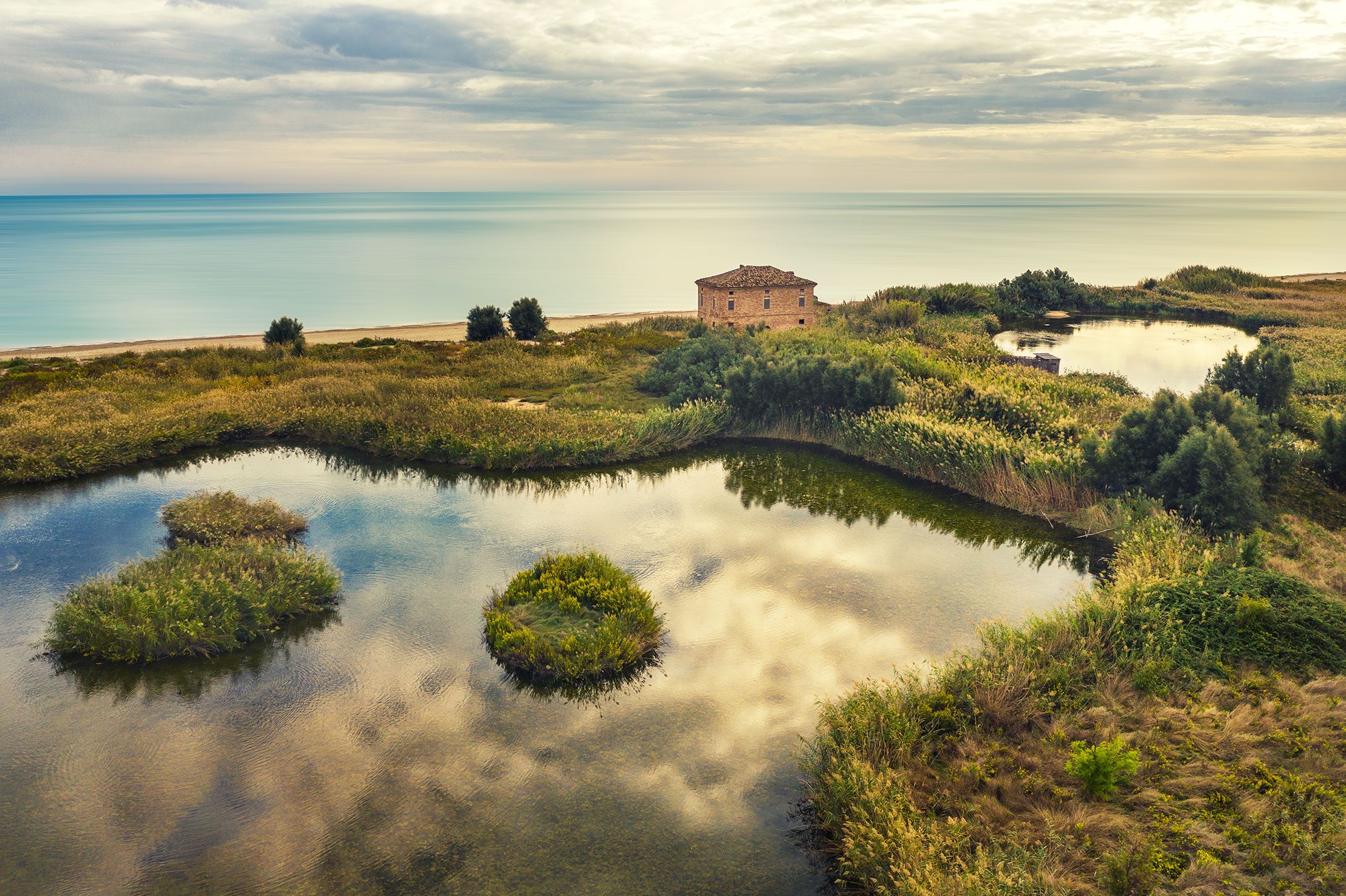 Steinhaus zwischen Wasserflächen an der Adriaküste im Morgenlicht, Italien