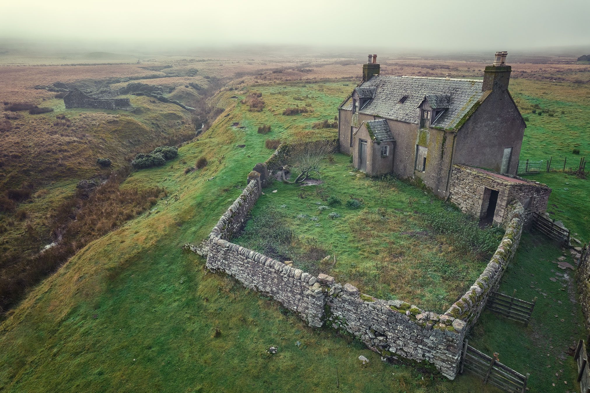Bauernhaus mit ummauertem Garten in nebliger Moorlandschaft, Schottland