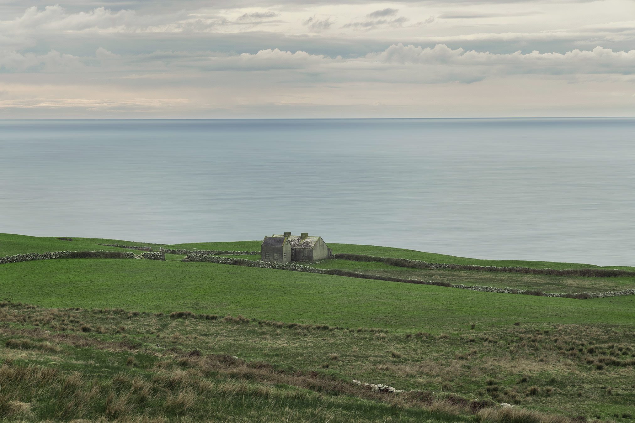 Einzelnes Haus auf einer grünen Steilküste über dem Atlantik, Irland