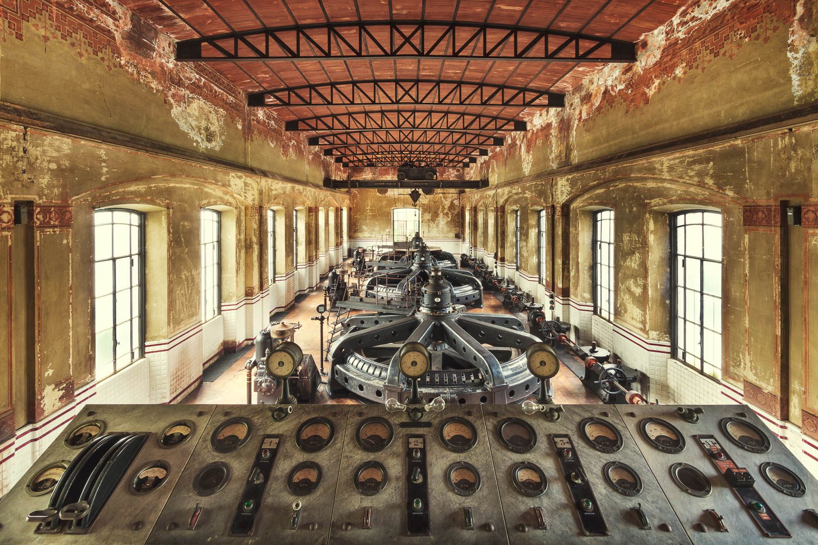 Switch panel in front of a row of black turbines in an abandoned hydroelectric plant in Italy