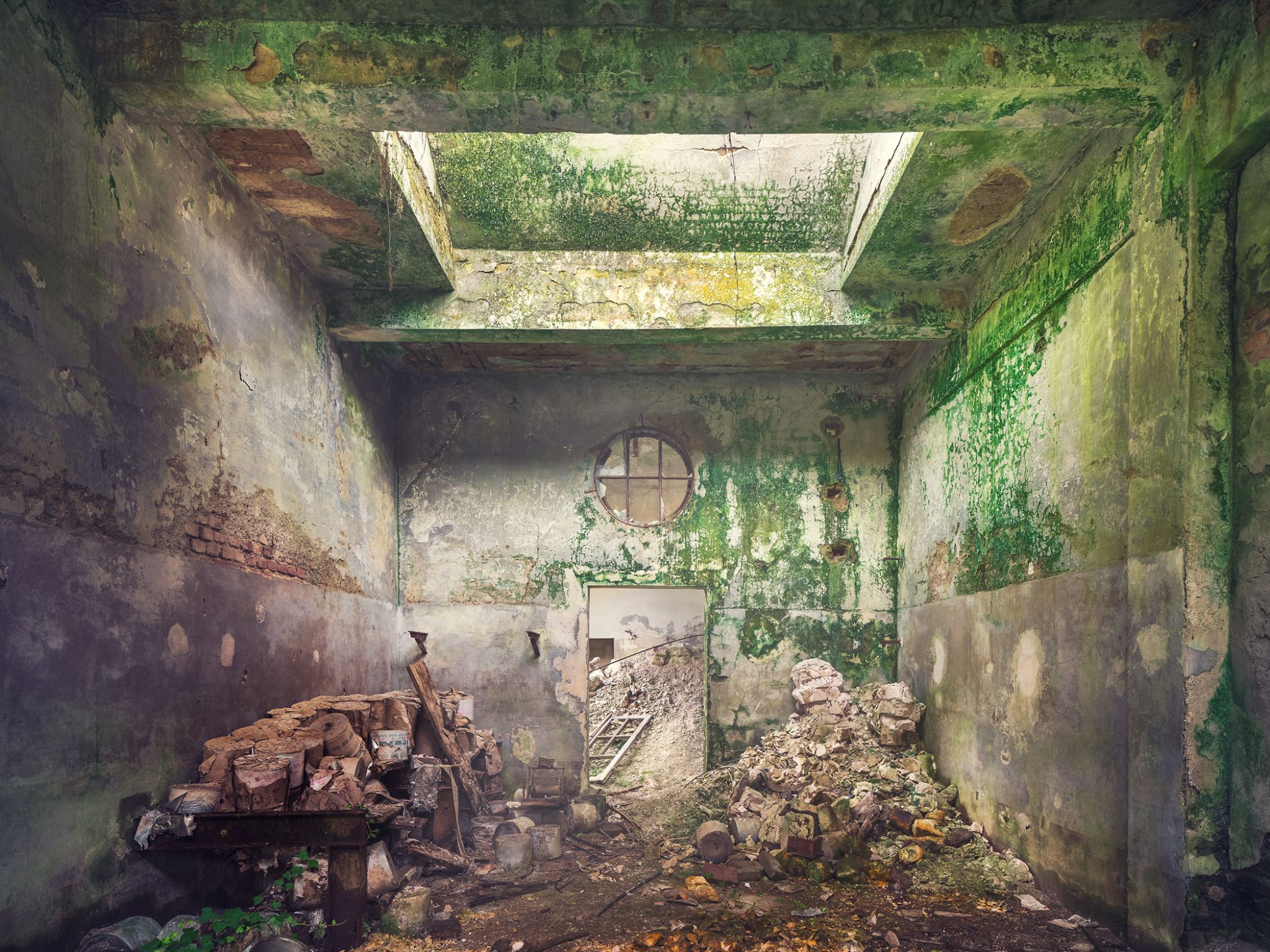 Moss-covered room with a round window in a decayed factory for medical products in Italy