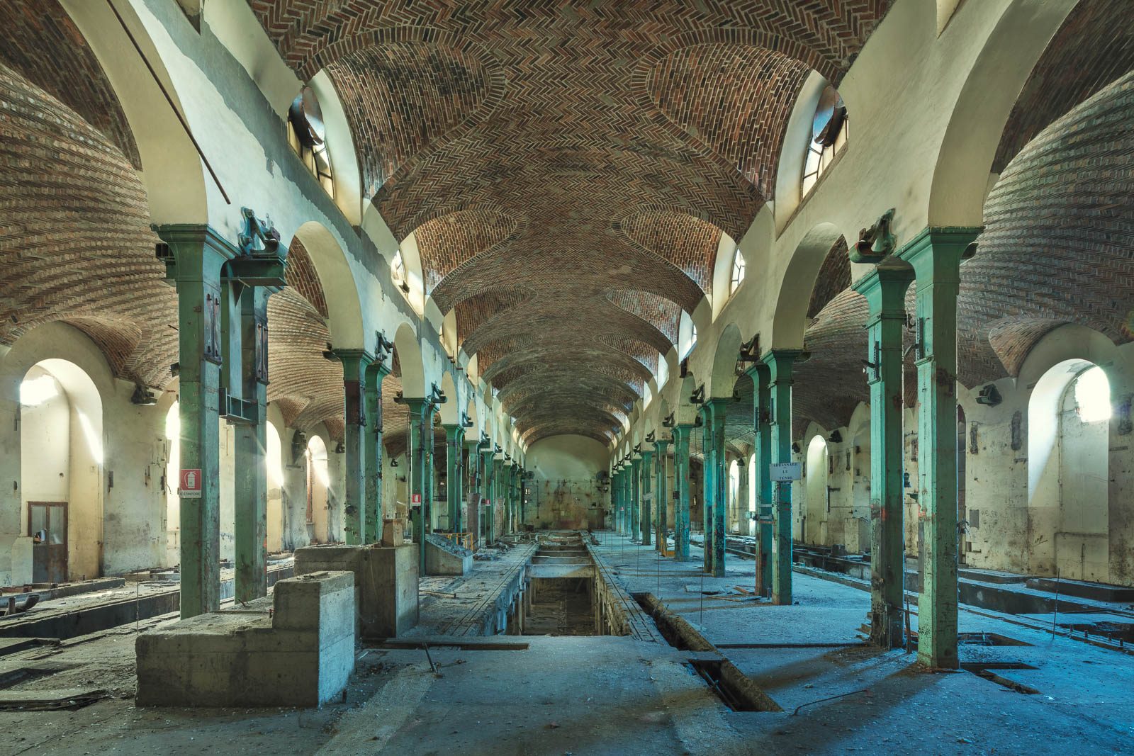 Cathedral-like hall with a brick vault and green cast-iron columns in a factory ruin