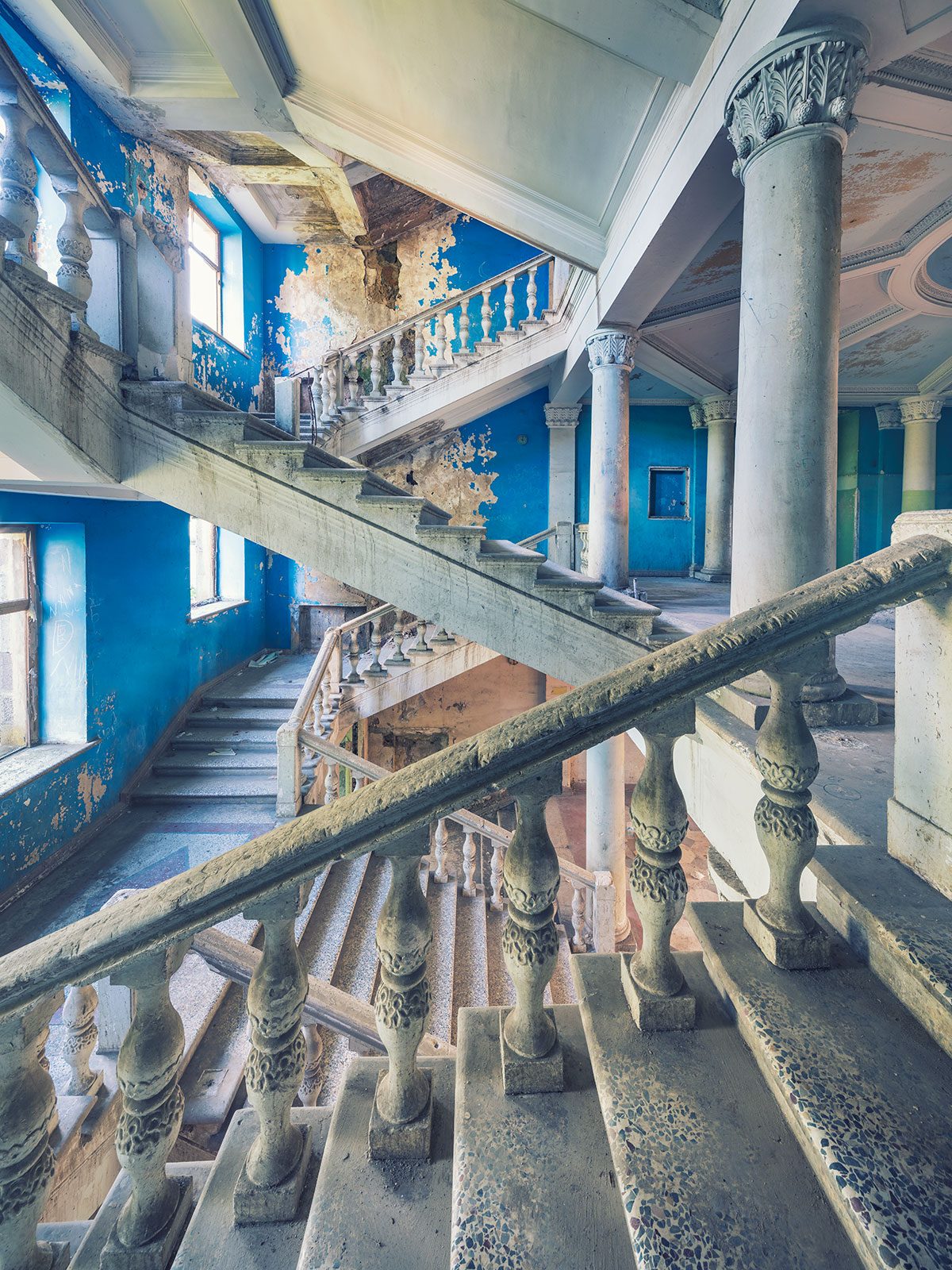 Staircase with columns before deep blue walls in an abandoned hotel in Georgia