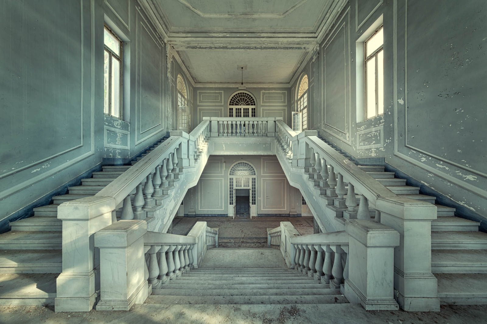 Symmetrische Doppeltreppe in einer blaugrau getünchten Halle einer psychiatrischen Anstalt in Italien