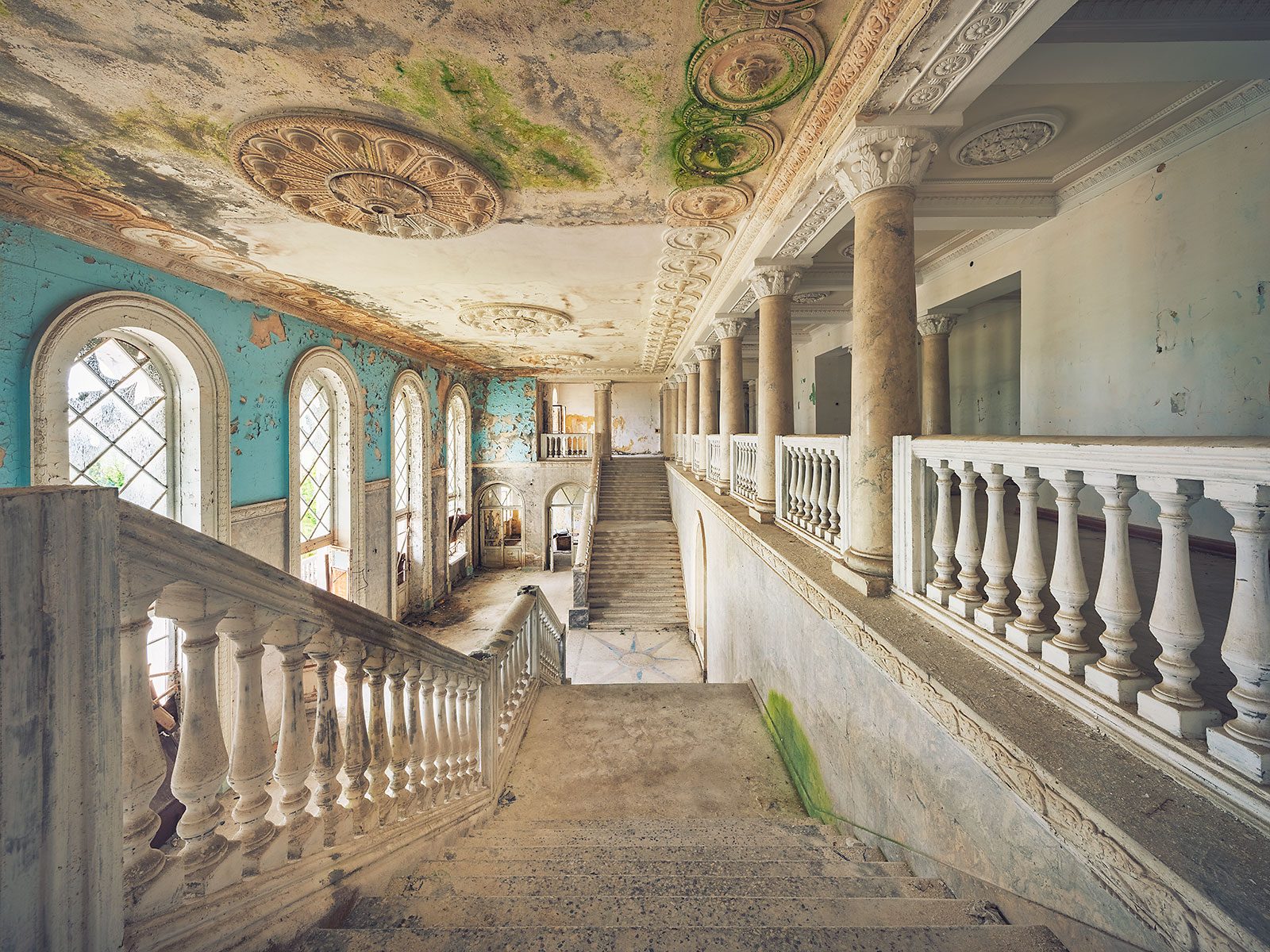 Treppenhaus mit Säulen und bemoosten Deckenrosetten in einem verlassenen Sanatorium in Georgien