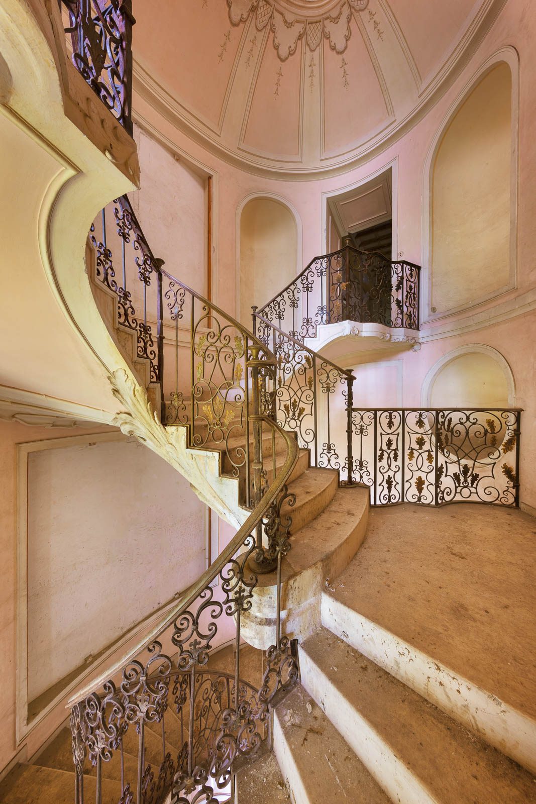 Geschwungene Treppe in einer rosafarbenen Rotunde in einer verlassenen Villa in Italien
