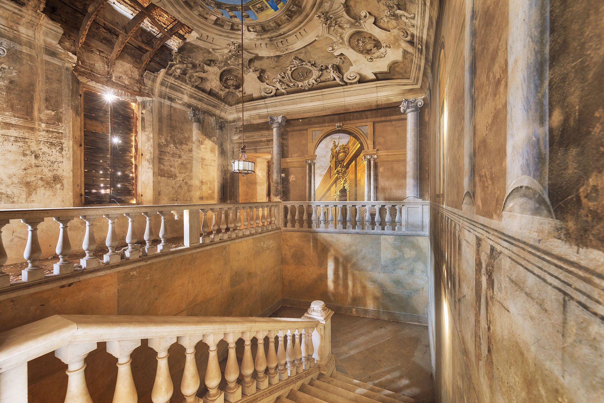 Staircase with a richly ornamented stucco ceiling in a forgotten palazzo in Italy
