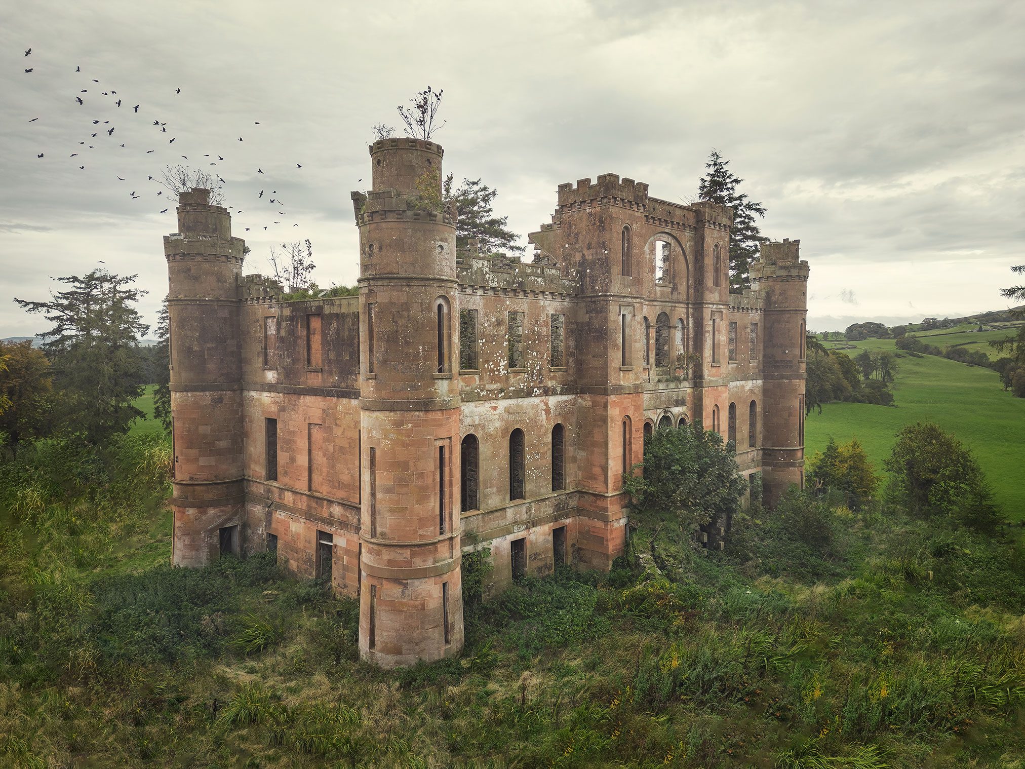 Ruin of a red sandstone castle with round towers and a flock of birds overhead, Scotland