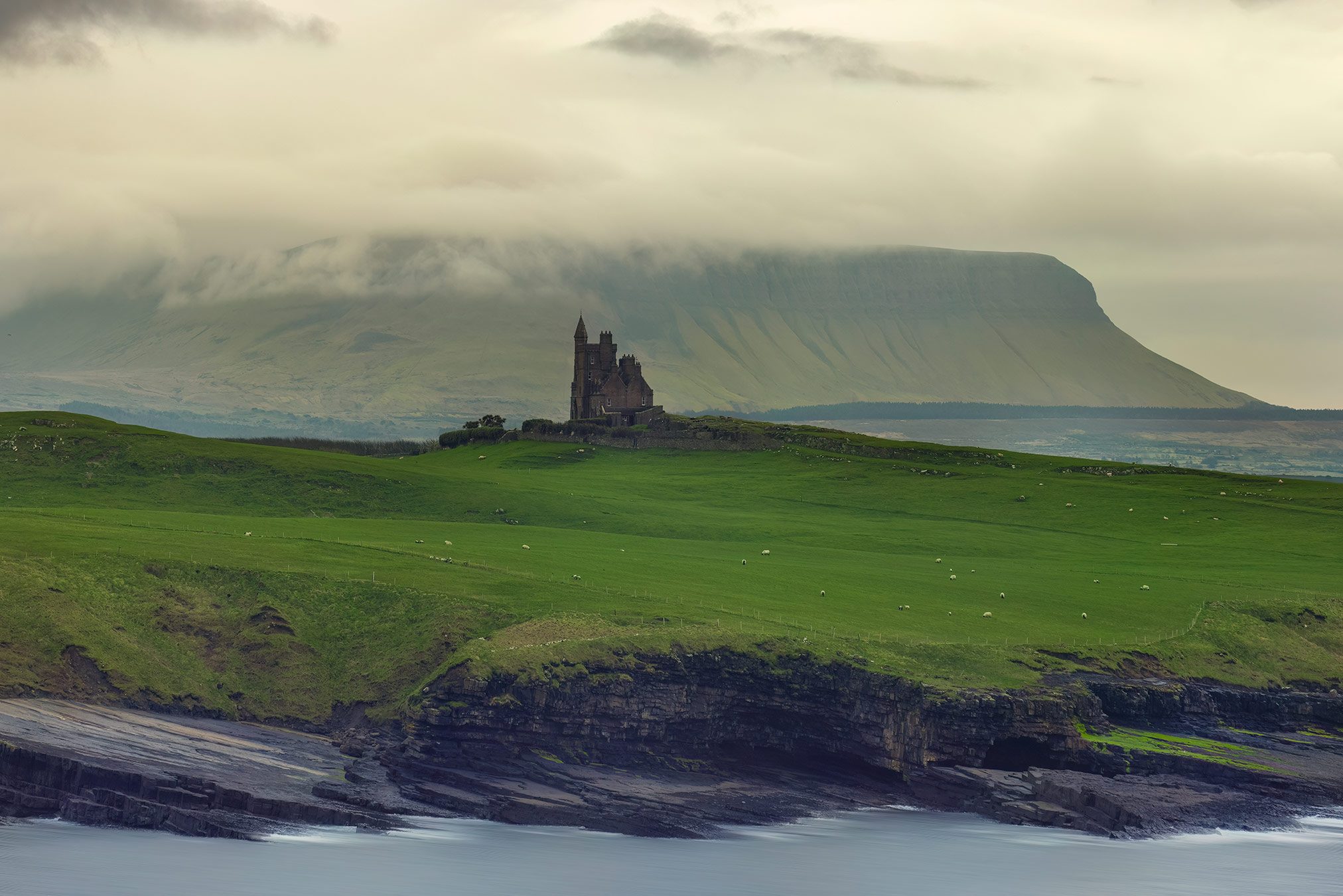 Manor house with a tower on a hilltop before a flat topped mountain, Ireland
