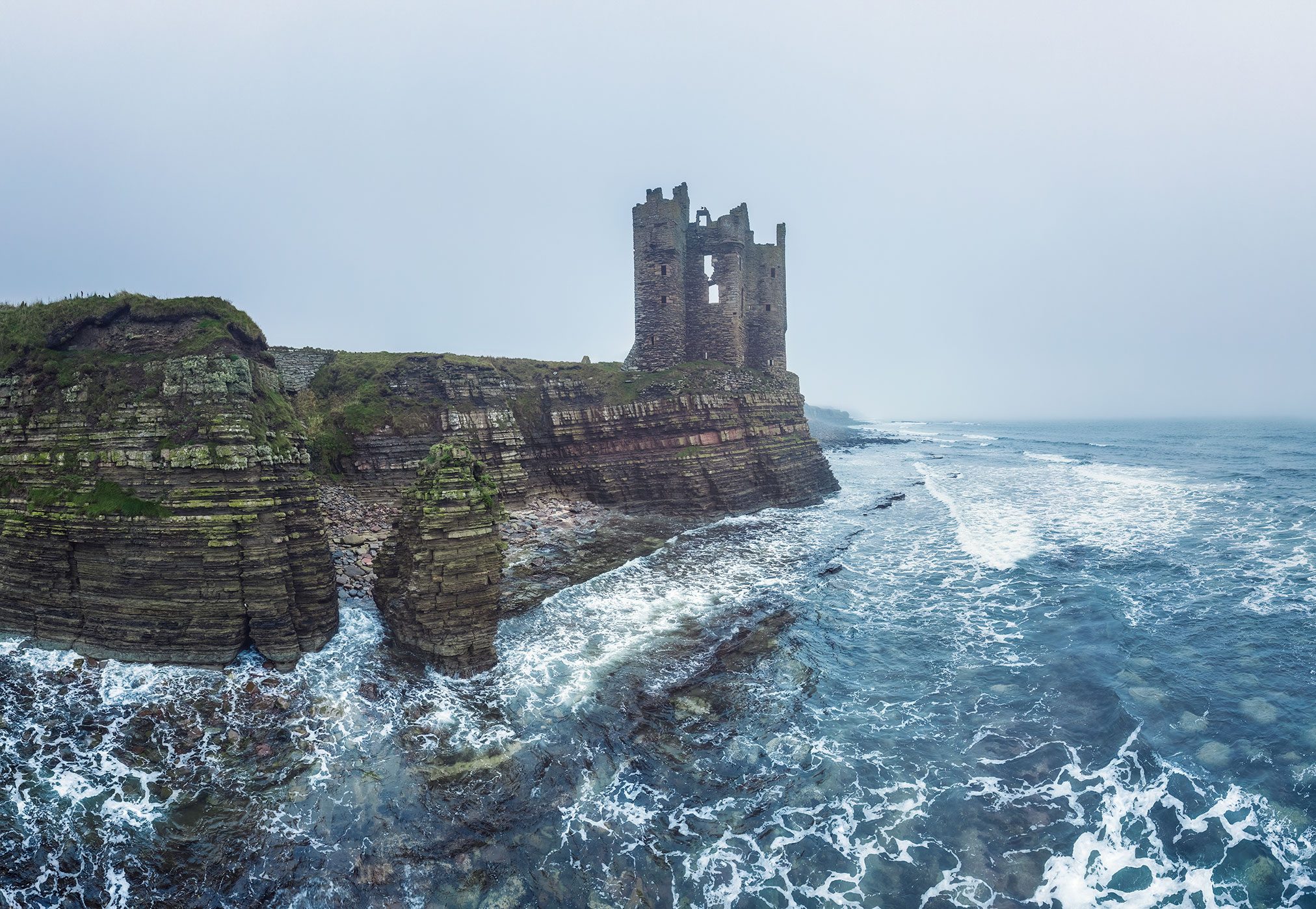 Tower ruin on a sea cliff in fog, Scotland