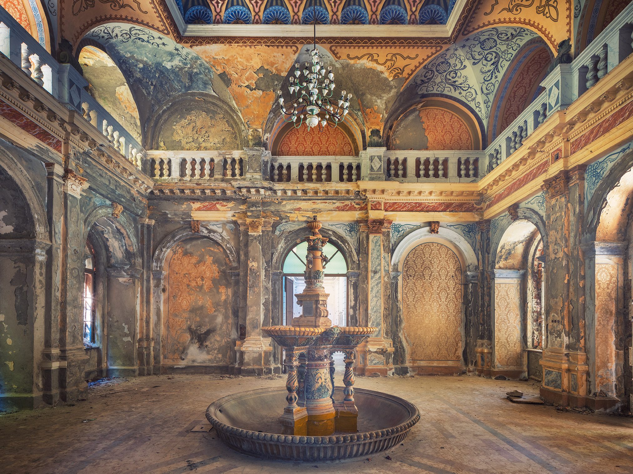 Oval hall with a painted dome, chandelier, and large fan-shaped window in a derelict spa building in Romania