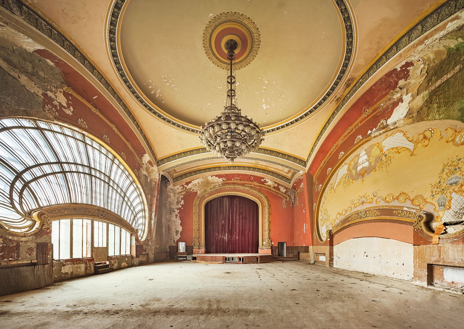 Oval hall with a painted vault, a chandelier, and a fan window in a decaying casino in Romania