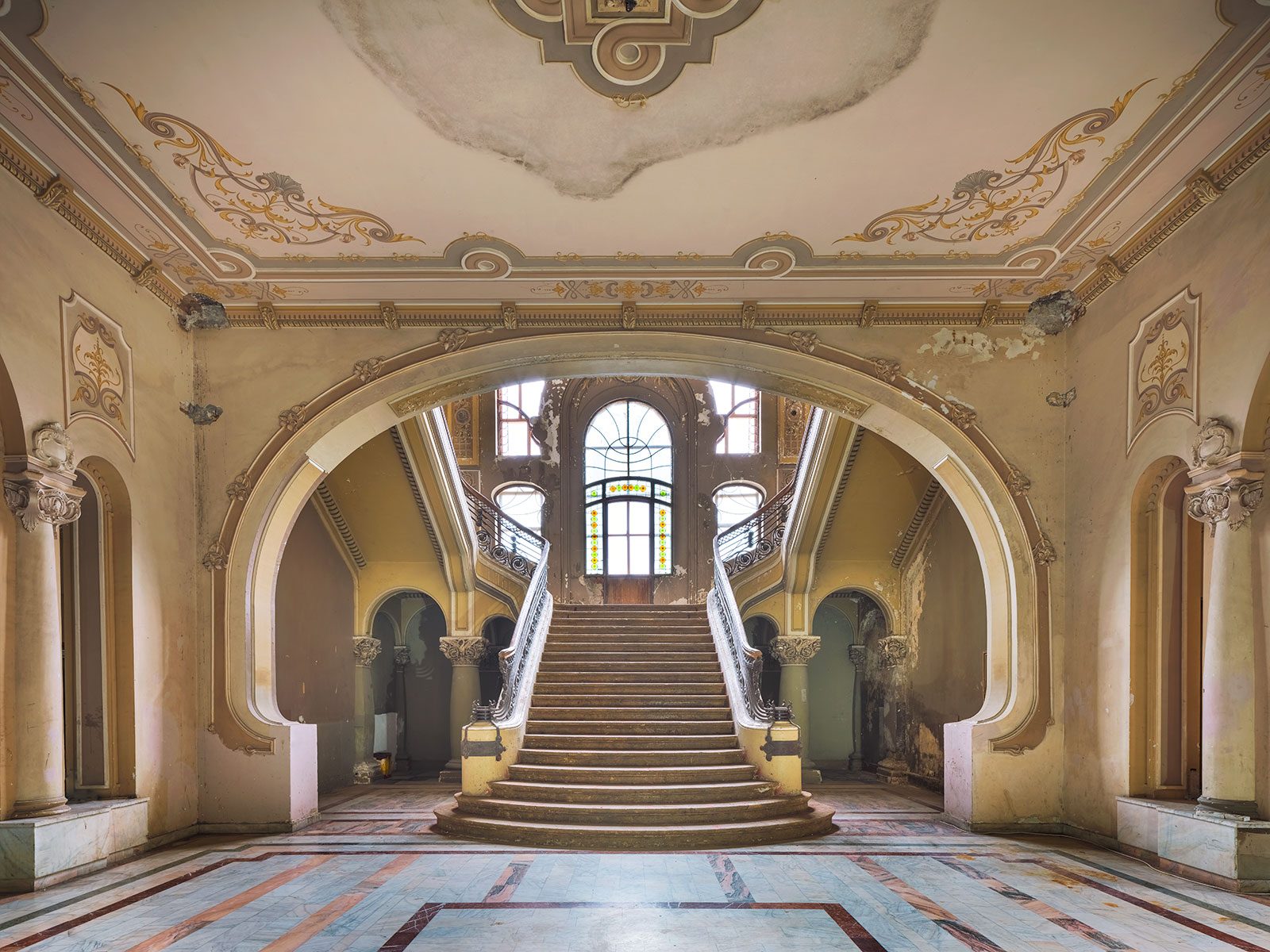 Double-flight marble staircase leading to a stained-glass window in a decaying casino in Romania